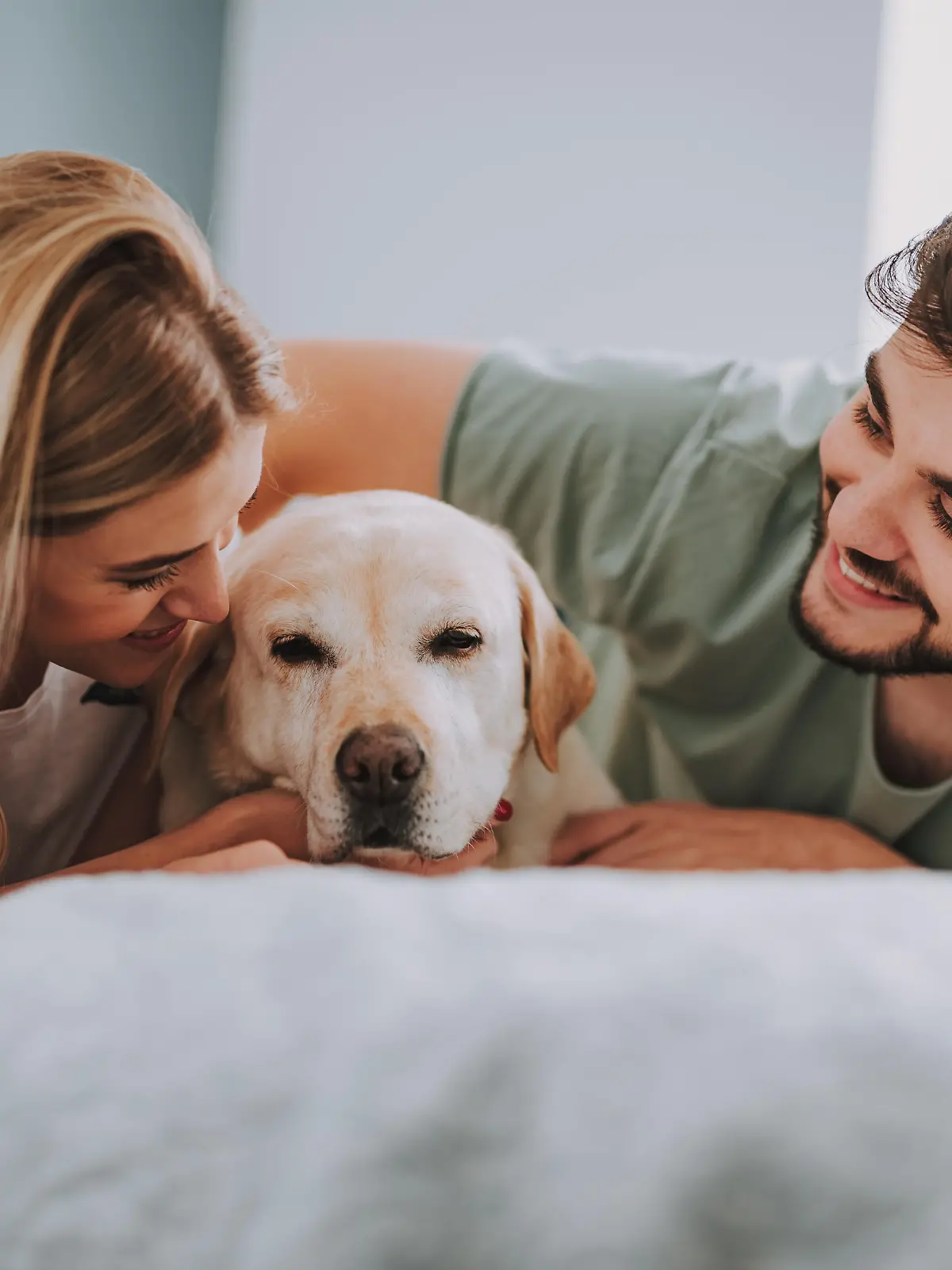Optimistic young couple lying in bed while having fun with their dog