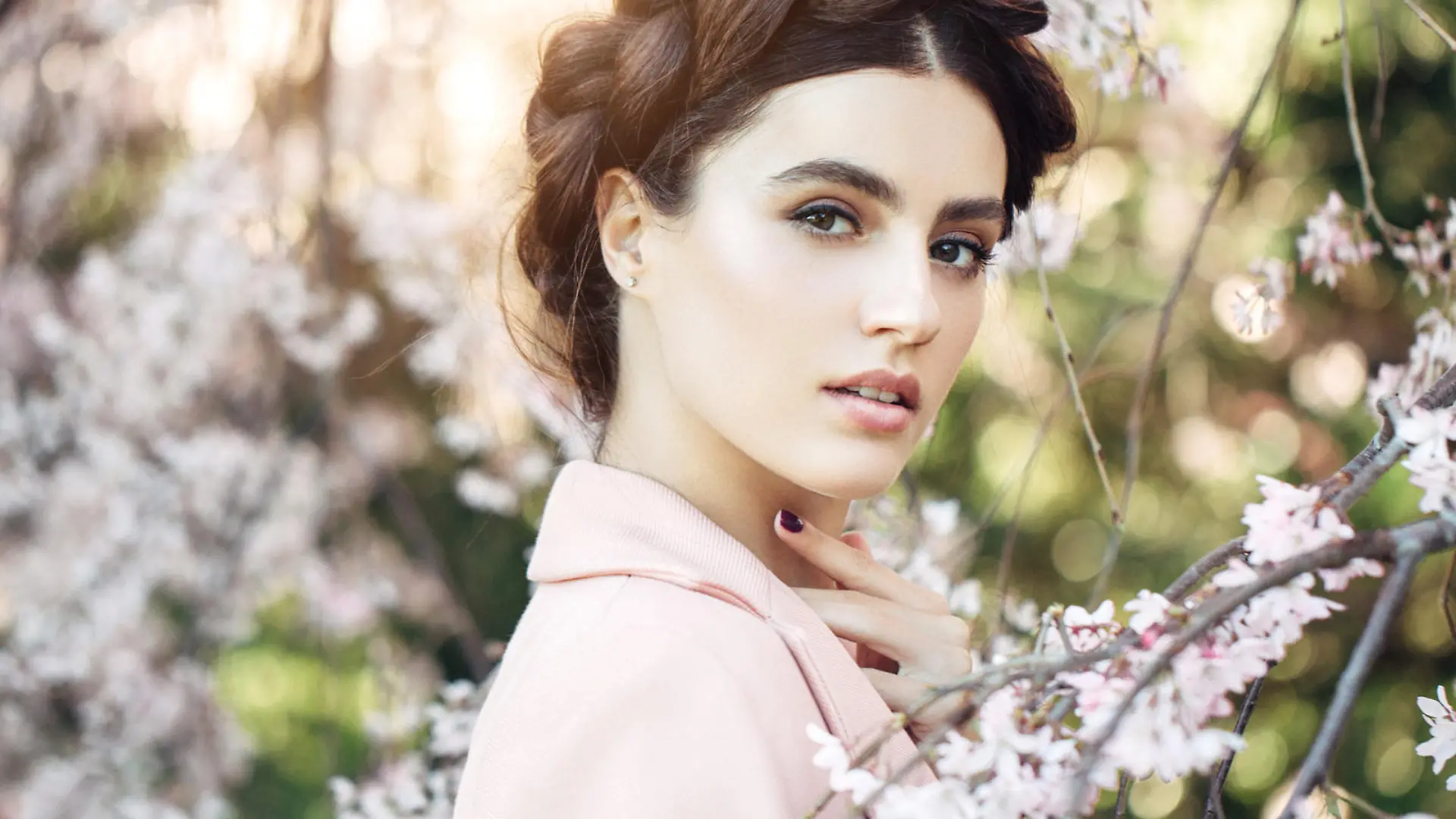Beautiful girl in the rays of sunset light on the background of spring bush