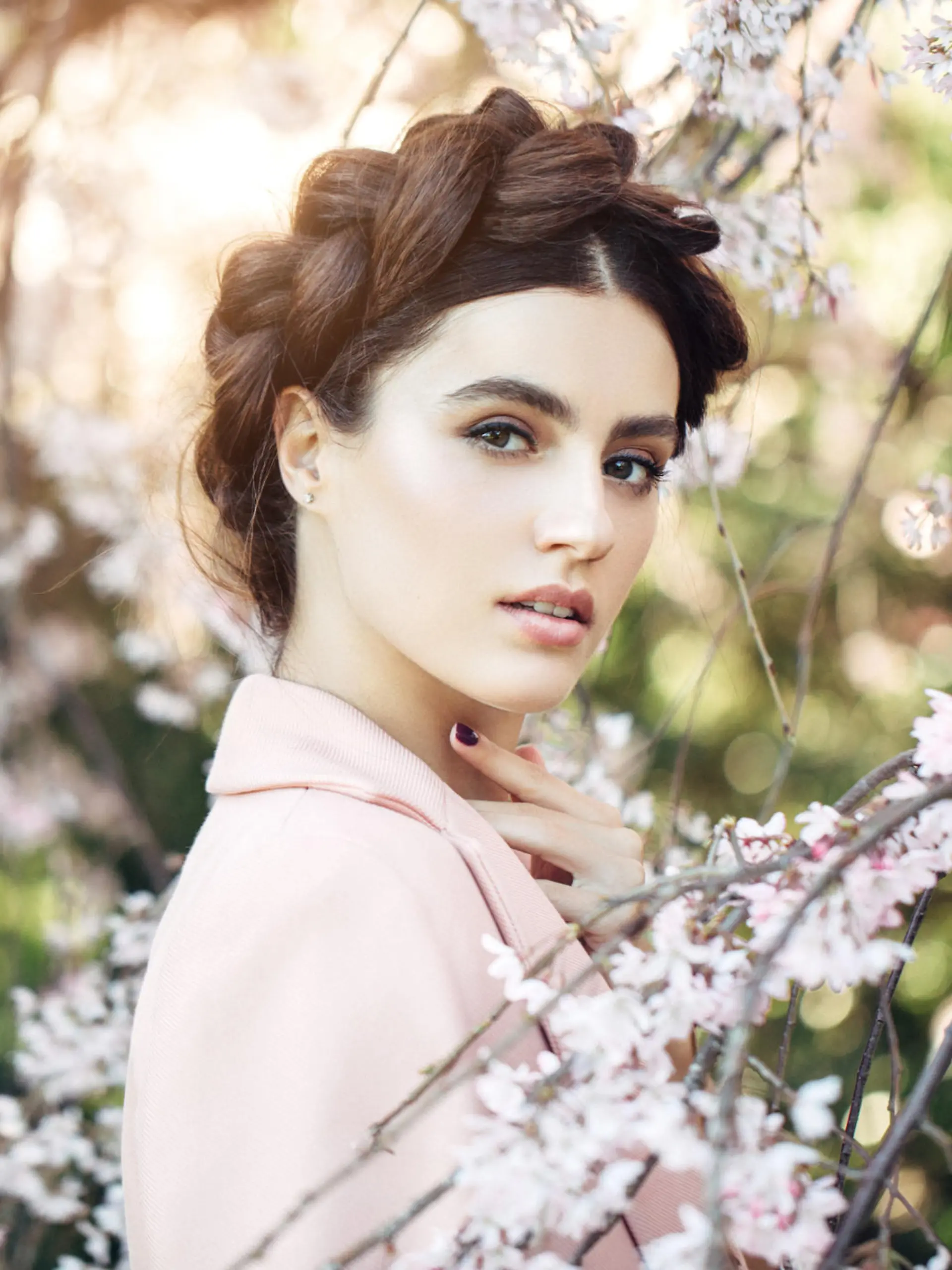 Beautiful girl in the rays of sunset light on the background of spring bush