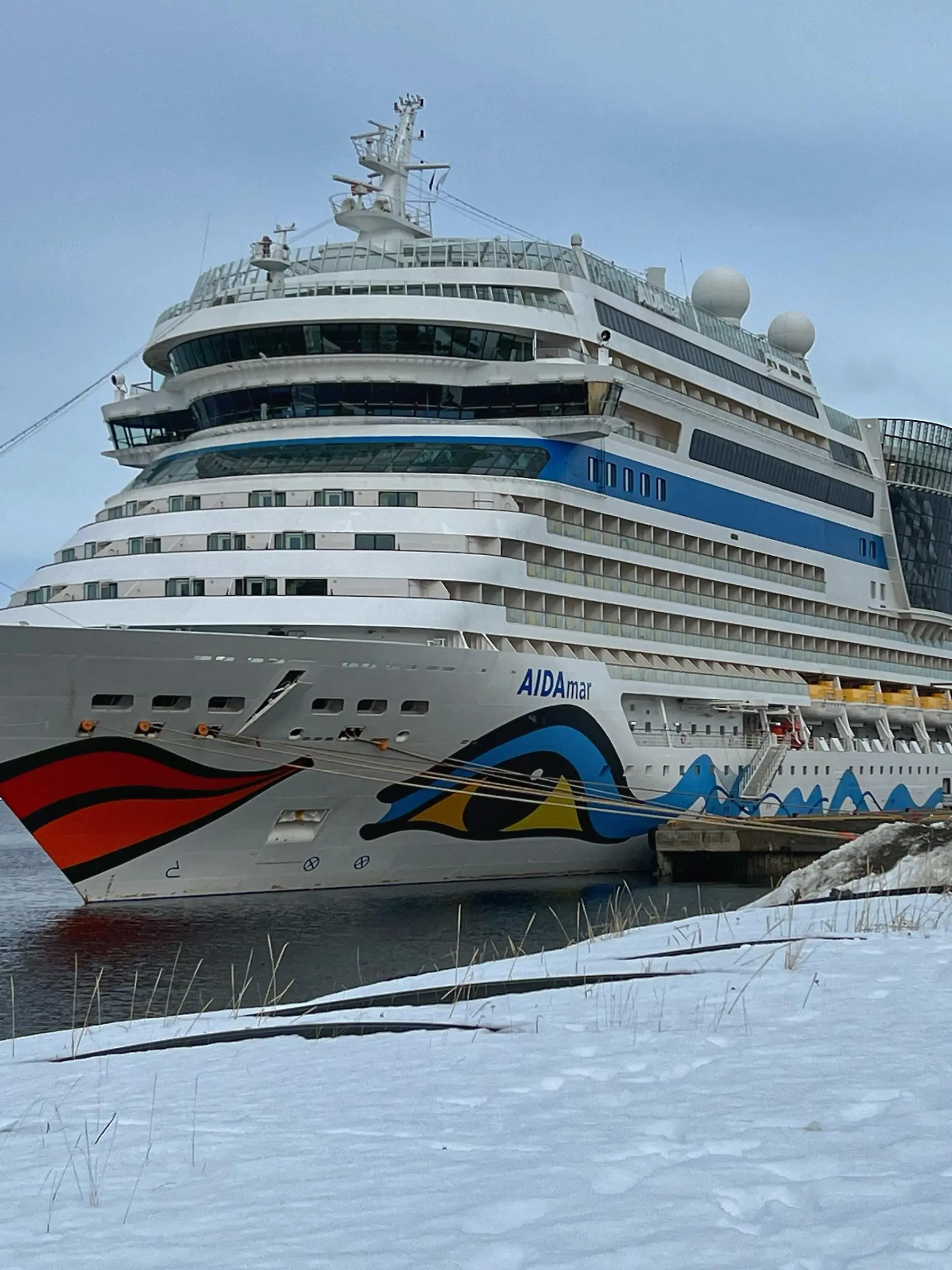 Das Kreuzfahrtschiff Aida mar liegt Karfreitag 2023 im Hafen von Alta (Norwegen). Der restliche Schnee des endenden Winters türmt sich vor dem Kreuzfahrtriesen.