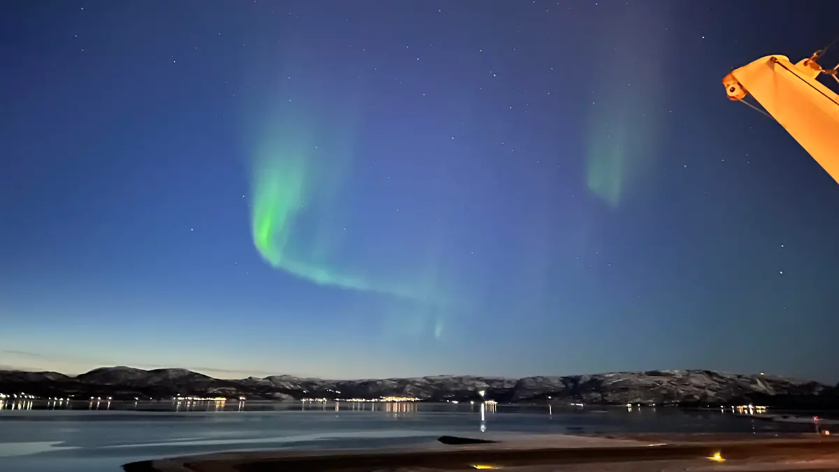 Ein grüner Lichtschweif am Himmel über dem Hafen von Alta in Norwegen. Der Ort ist bekannt für Nordlichter (auch Polarlichter genannt).