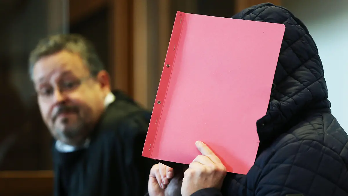 06.10.2020, Nordrhein-Westfalen, Köln: Der Angeklagte (r) im Prozess wegen schweren sexuellen Missbrauchs von Kindern sitzt Gerichtssaal, während er sich eine Mappe vor das Gesicht hält. Im Hintergrund sitzt der Anwalt des Angeklagten. Im Missbrauchskomplex Bergisch Gladbach ist der Angeklagte zu zwölf Jahren Haft verurteilt worden. Foto: Oliver Berg/dpa +++ dpa-Bildfunk +++