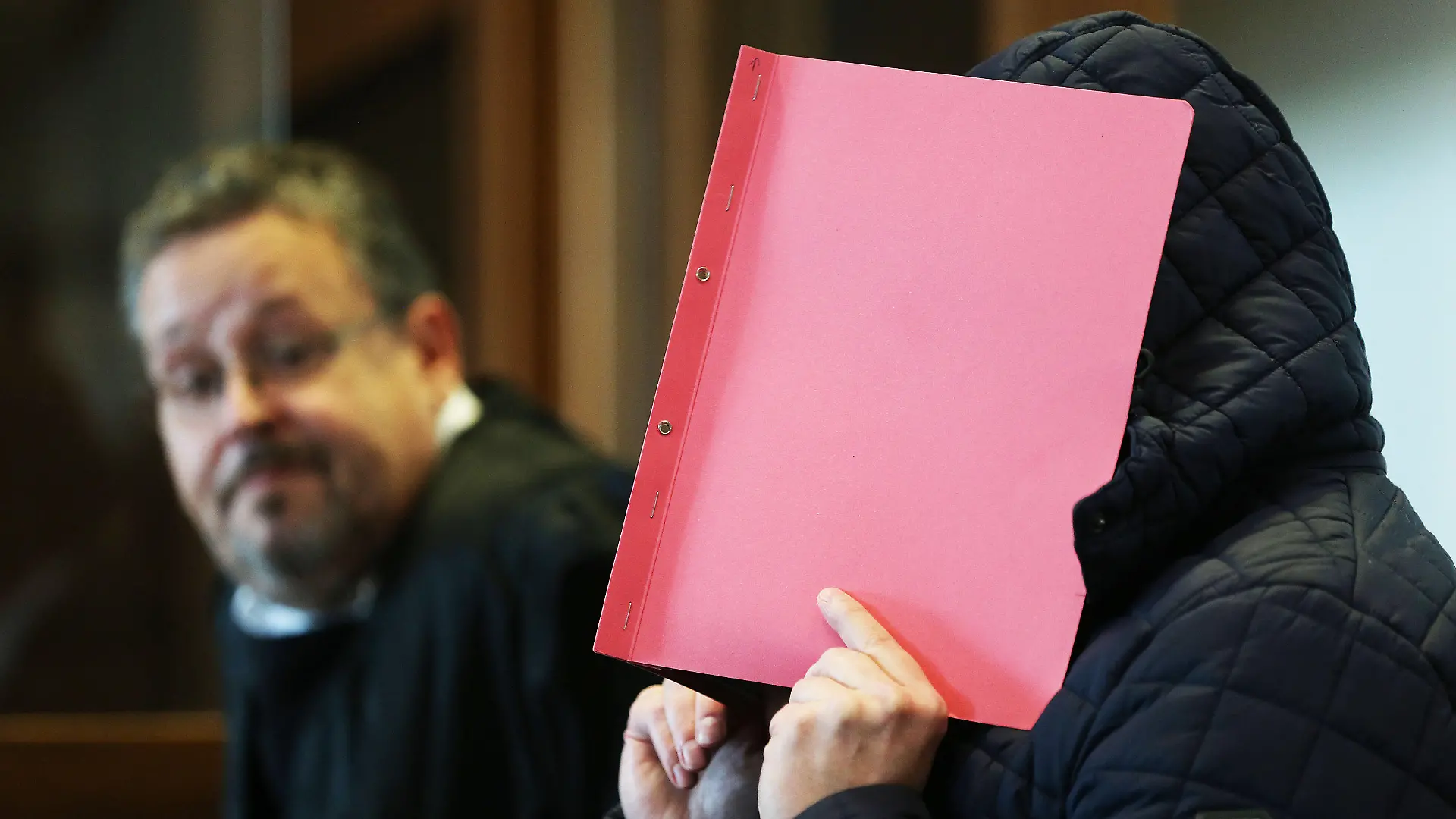 06.10.2020, Nordrhein-Westfalen, Köln: Der Angeklagte (r) im Prozess wegen schweren sexuellen Missbrauchs von Kindern sitzt Gerichtssaal, während er sich eine Mappe vor das Gesicht hält. Im Hintergrund sitzt der Anwalt des Angeklagten. Im Missbrauchskomplex Bergisch Gladbach ist der Angeklagte zu zwölf Jahren Haft verurteilt worden. Foto: Oliver Berg/dpa +++ dpa-Bildfunk +++