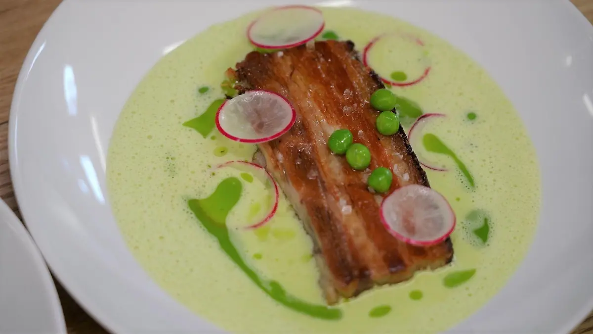 Der knusprige Schweinebauch liegt in einem Erbsenschaumsüppchen-Bett aus Erbsen, Spargel und Bärlauchöl.