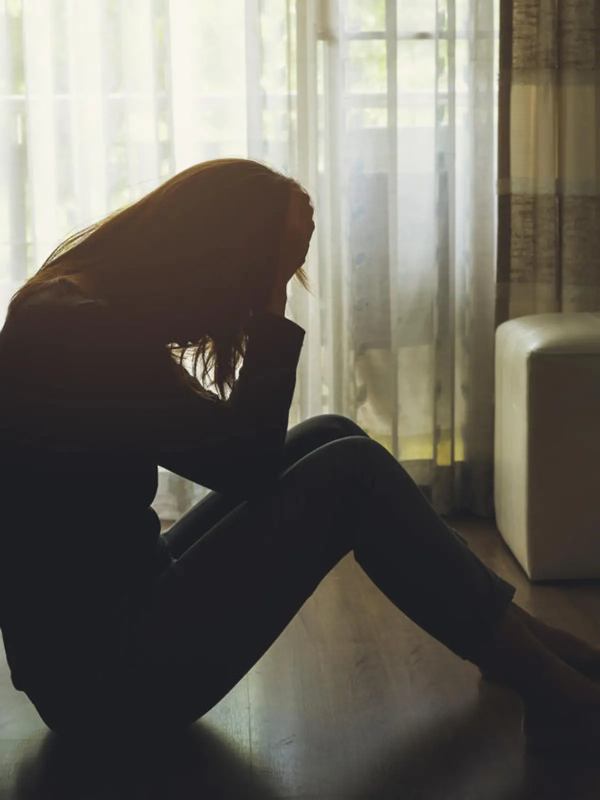 depressed woman sitting head in hands in the dark bedroom