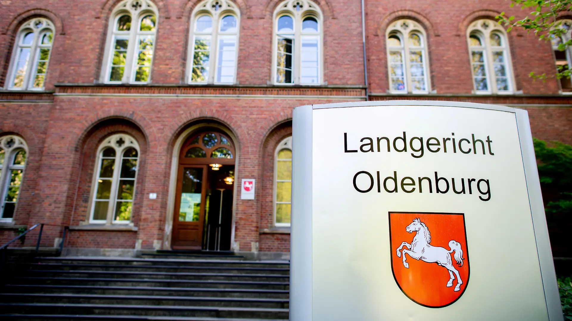 09.05.2022, Niedersachsen, Oldenburg: Ein Schild mit dem niedersächsischen Landeswappen steht vor dem Eingang zum Landgericht Oldenburg, wo ein Prozess wegen zweifachen Mordes fortgesetzt wird. Der angeklagte Mann soll im Oktober 2021 in Delmenhorst zunächst in einer Bar einen vermeintlichen Nebenbuhler erstochen haben. Anschließend verletzte er seine Lebensgefährtin mit einem Messer so stark, dass sie zwei Tage später starb. Foto: Hauke-Christian Dittrich/dpa +++ dpa-Bildfunk +++