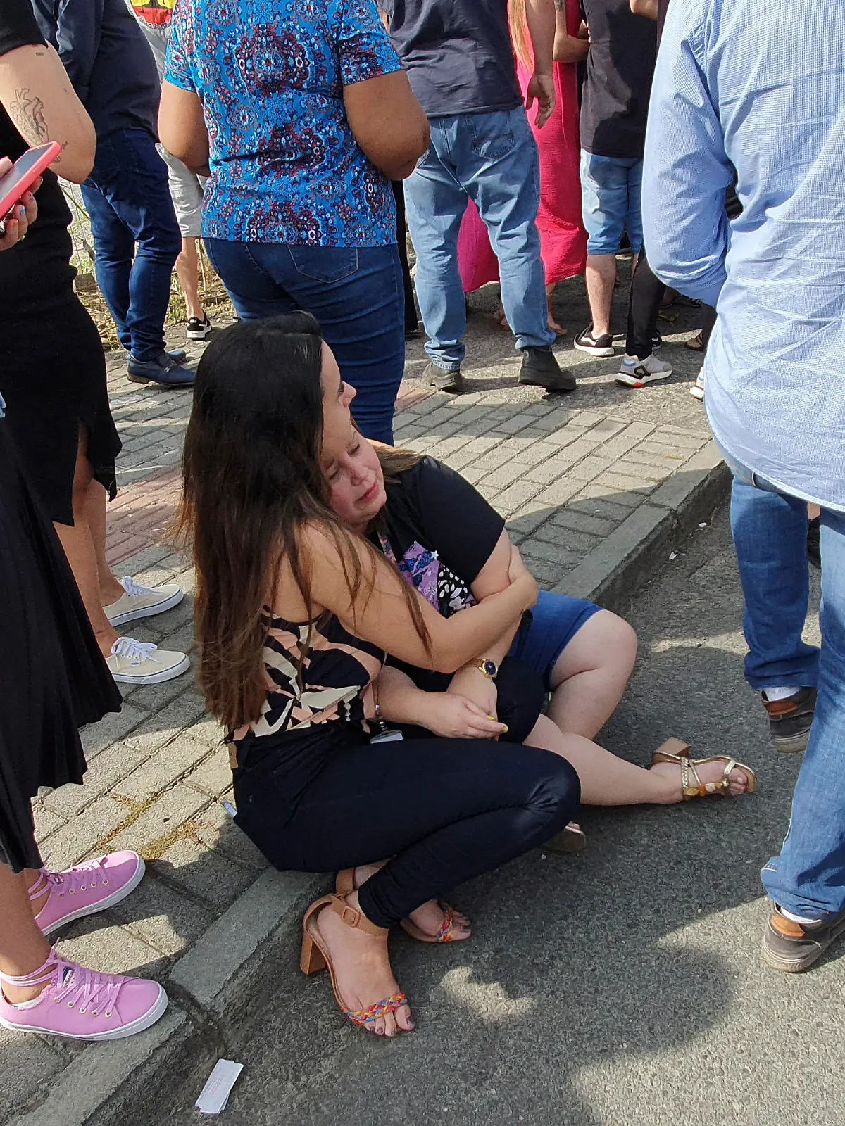 05.04.2023, Brasilien, Blumenau: Eine Frau und ein Mädchen sitzen vor der Kinderkrippe «Cantinho do Bom Pastor» nach einem tödlichen Angriff. Ein 25-Jähriger war nach Angaben der Militärpolizei am Mittwochmorgen in die private Kinderkrippe in Blumenau, das von deutschen Einwanderern gegründet und geprägt wurde, eingedrungen und hatte Kinder angegriffen. Foto: Patrick Rodrigues/POrtal NSC Total/dpa +++ dpa-Bildfunk +++