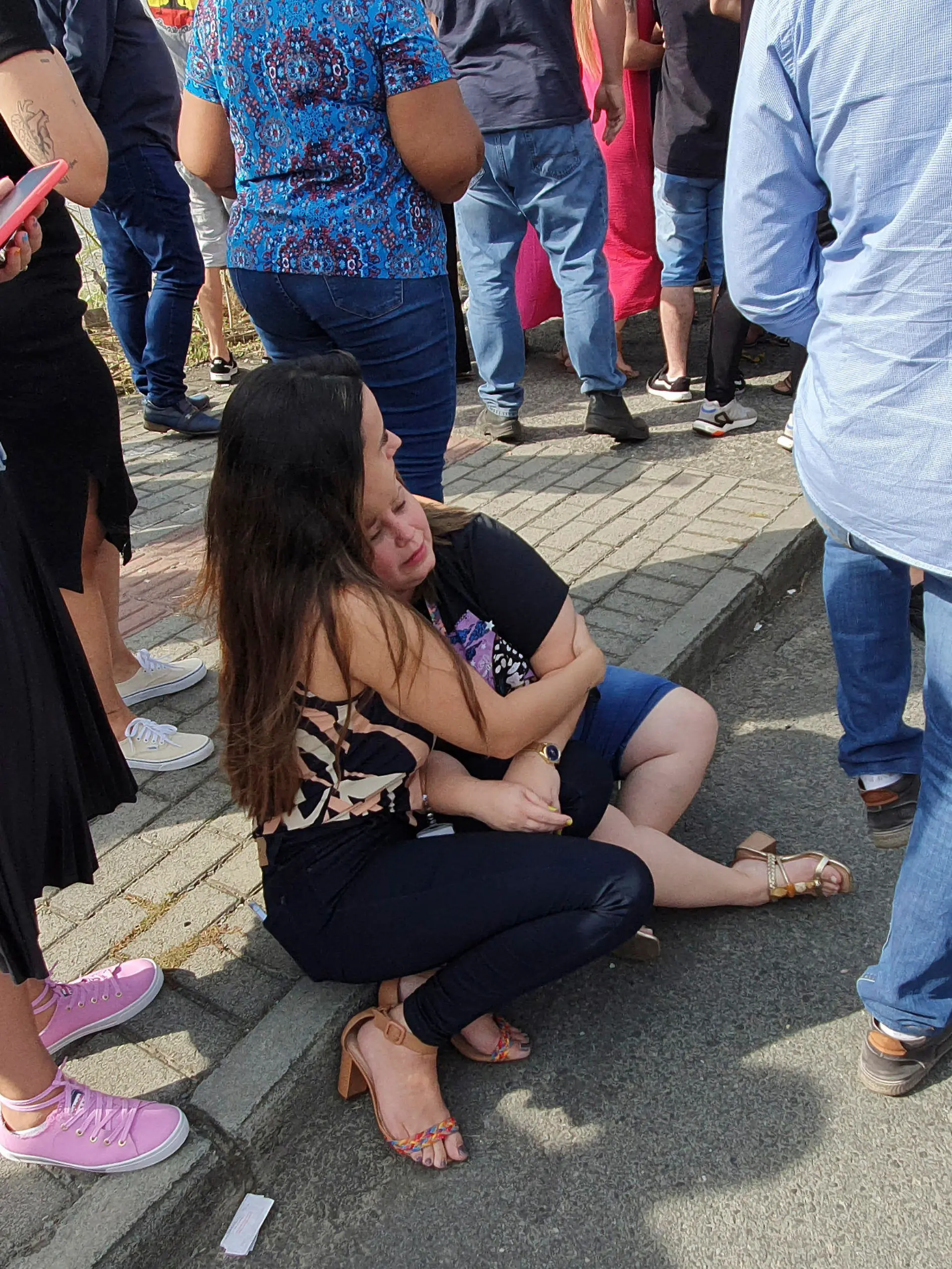 05.04.2023, Brasilien, Blumenau: Eine Frau und ein Mädchen sitzen vor der Kinderkrippe «Cantinho do Bom Pastor» nach einem tödlichen Angriff. Ein 25-Jähriger war nach Angaben der Militärpolizei am Mittwochmorgen in die private Kinderkrippe in Blumenau, das von deutschen Einwanderern gegründet und geprägt wurde, eingedrungen und hatte Kinder angegriffen. Foto: Patrick Rodrigues/POrtal NSC Total/dpa +++ dpa-Bildfunk +++