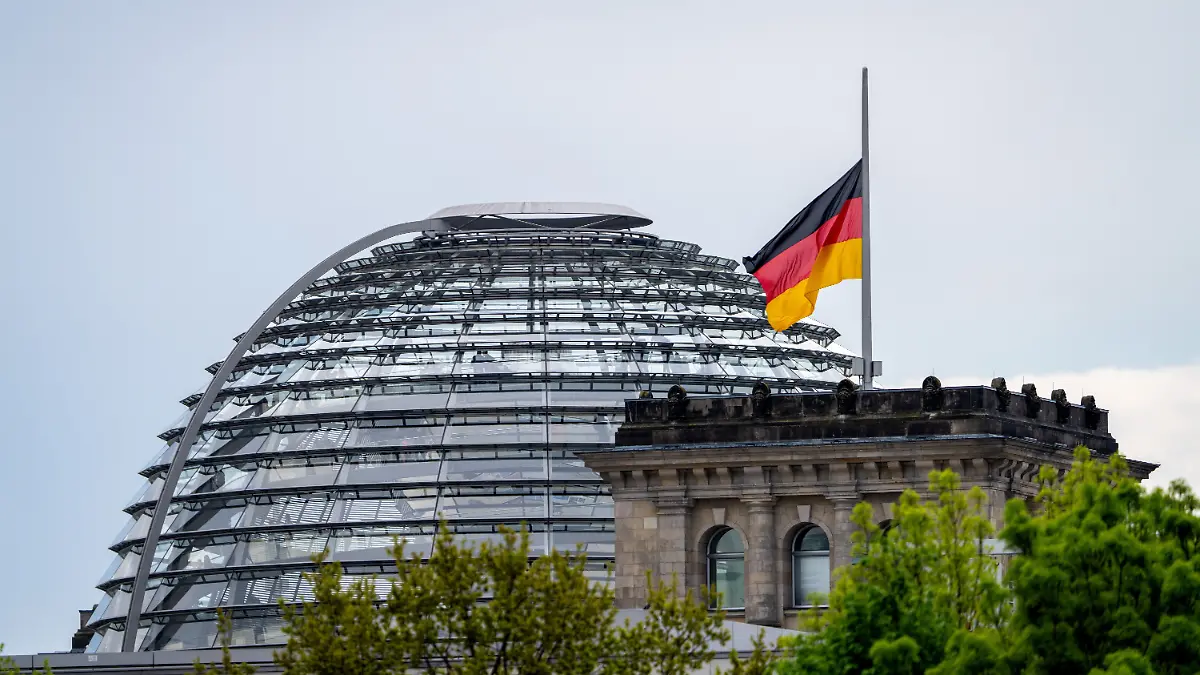 Eine der Deutschland-Flaggen auf dem Reichstag weht am Morgen vor der Kulisse der Reichstagskuppel auf Halbmast.