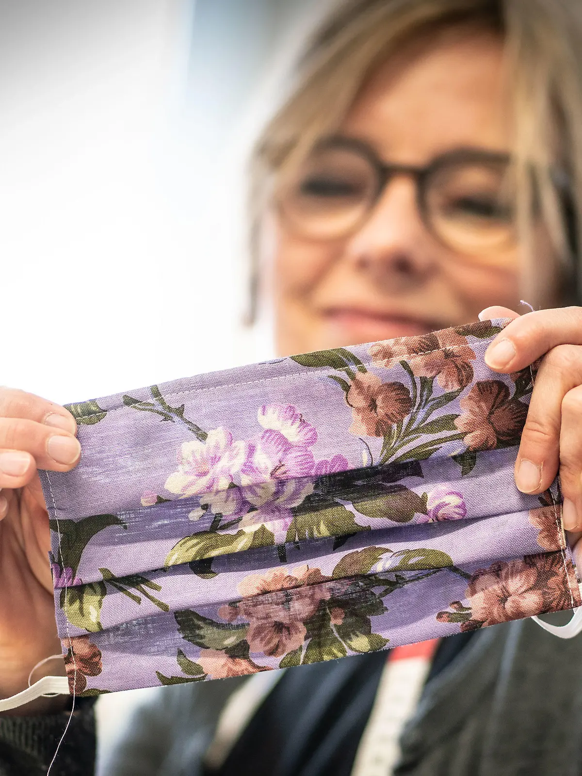 24.03.2020, Hessen, Frankfurt/Main: Fachanleiterin Kerstin Jentschke vom "Cariteam" der Caritas Frankfurt zeigt ihre soeben fertig gestellte Mundschutzmaske. Zur Zeit näht sie mit ihren Kolleginnen die auskochbaren Masken aus bunten Baumwollstoffen selbst. Diese werden zum Beispiel dringend in der Altenpflege benötigt . Normalerweise können im "Cariteam" Langzeitarbeitslose, Asylbewerber oder Geflüchtete berufliche Erfahrungen sammeln. Foto: Frank Rumpenhorst/dpa +++ dpa-Bildfunk +++