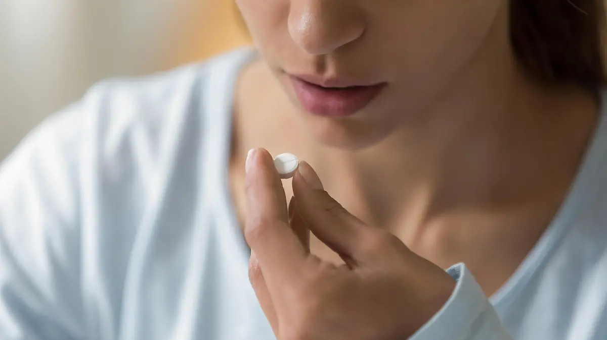 Closeup image of woman face and pill in hand. Sick young female holding white round pill near her mouth and going to take medication as per doctor prescription for recovery. Healthcare medical concept