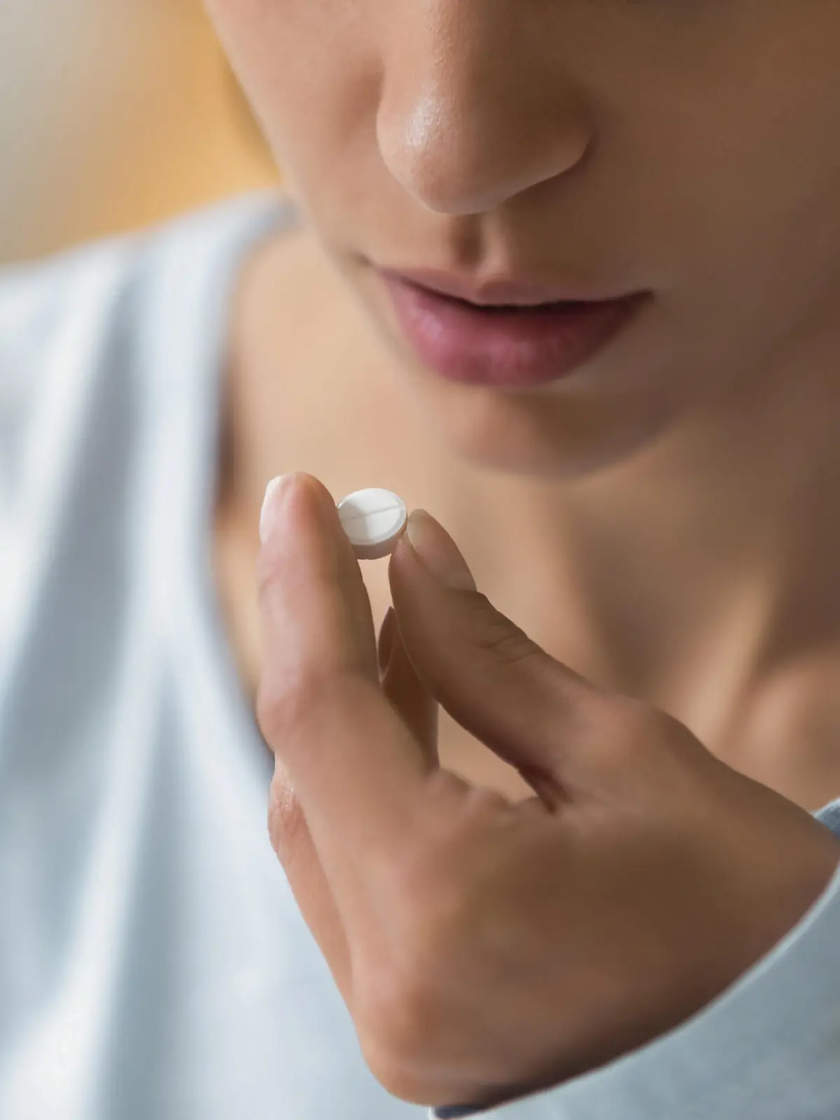 Closeup image of woman face and pill in hand. Sick young female holding white round pill near her mouth and going to take medication as per doctor prescription for recovery. Healthcare medical concept