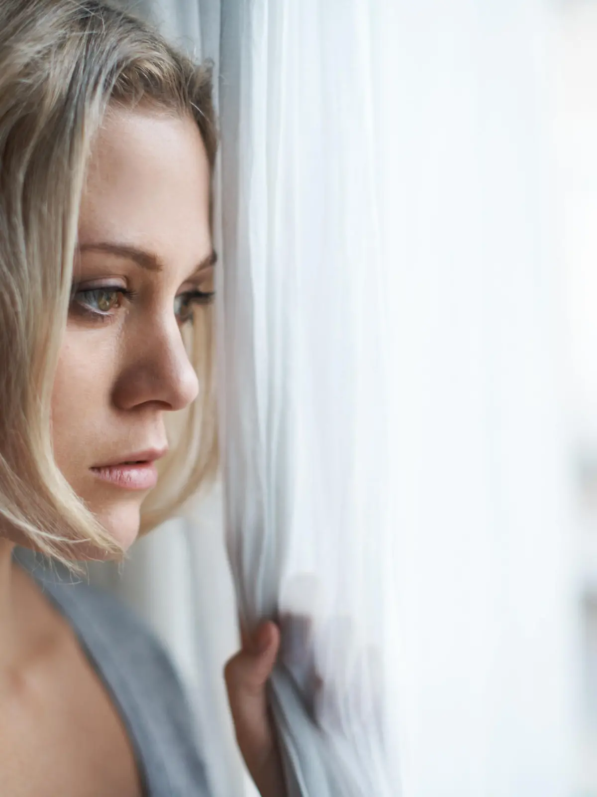 A beautiful young blonde woman looking out of her window sadly