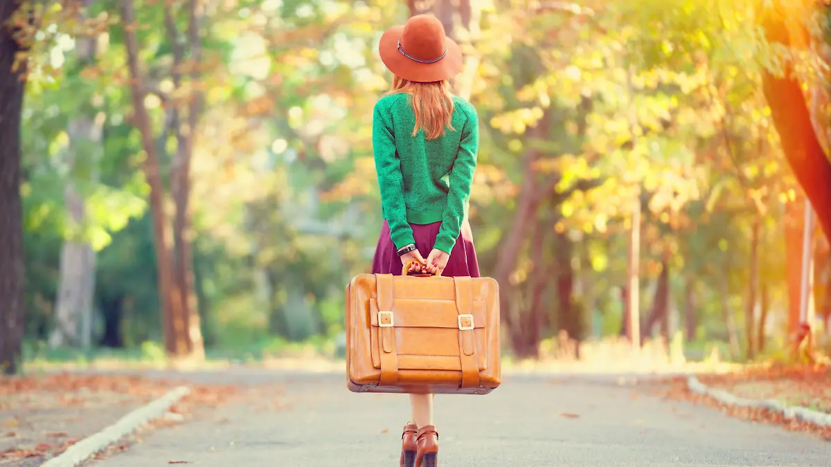Beautiful redhead girl with suitcase in the park.