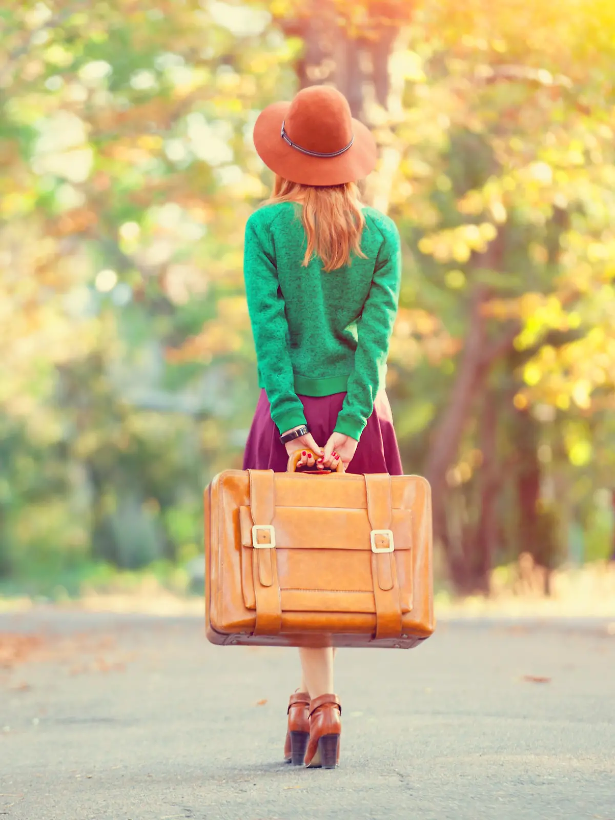 Beautiful redhead girl with suitcase in the park.