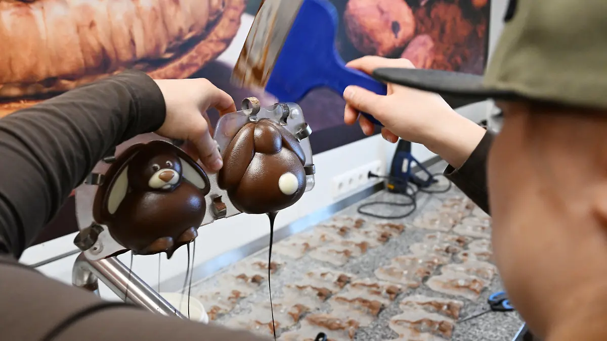 PRODUKTION - 30.03.2023, Bayern, Garmisch-Partenkirchen: Ein Konditorin gießt in der Chocolaterie Amelie eine «geschminkte» Osterhasen-Form mit Schokolade aus. Die Herstellung von Schoko-Osterhasen oder Schoko-Ostereiern ist hier in jedem Arbeitsschritt noch Handarbeit. (zu dpa: «Schokolade trotzt der Krisenstimmung - Fast 10 Kilo pro Kopf genascht») Foto: Angelika Warmuth/dpa +++ dpa-Bildfunk +++