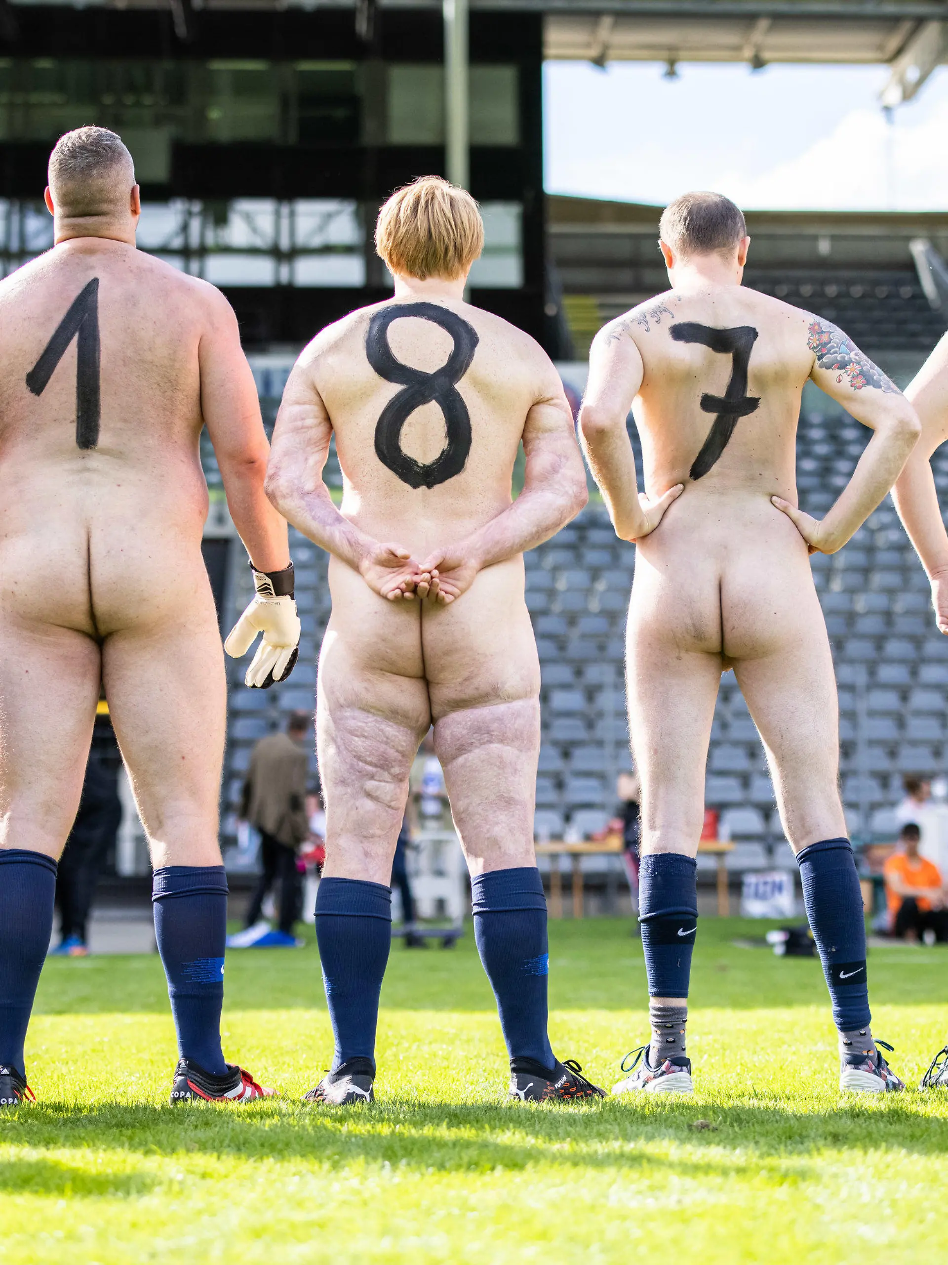 06.09.2020, Nordrhein-Westfalen, Wuppertal: Nackte Fußballer aus Deutschland stehen mit auf den Rücken gemalten Zahlen vor dem Spiel im Stadion am Zoo nebeneinander. Aus Protest gegen die aus ihrer Sicht zunehmende Kommerzialisierung des Profifußballs traten zwei Mannschaften nackt gegeneinander an. Organisator des Naked Fußball ist der Künstler Starczewski, der jeden Teilnehmer im Anschluss per Urkunde zum offiziellen Nacktionalspieler ernennen will. Foto: Marcel Kusch/dpa +++ dpa-Bildfunk +++