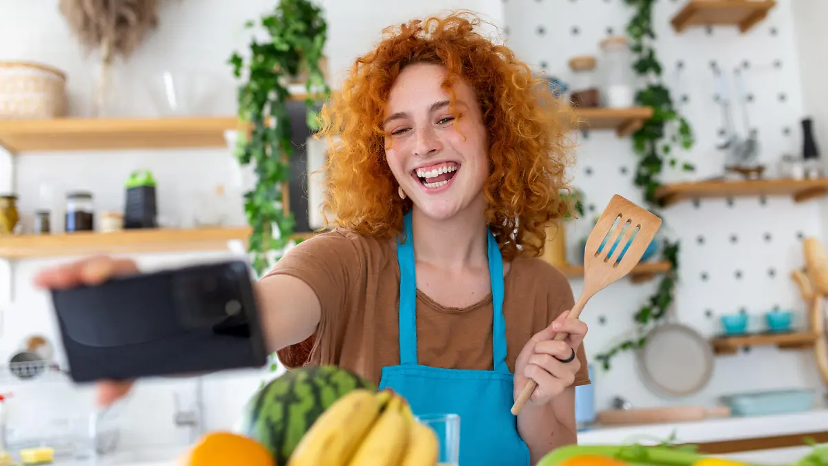 Frau, die in der Küche mit einem Kochlöffel in der Hand für ein Selfie posiert.