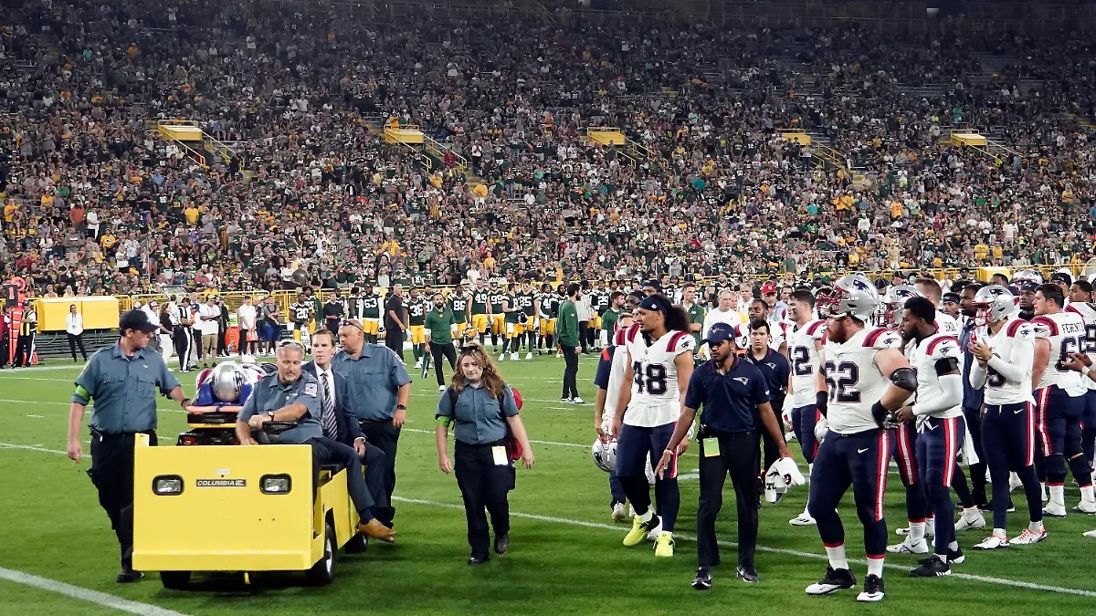 19.08.2023, USA, Green Bay: NFL; Vorbereitungsspiel; Testspiel; New England Patriots - Green Bay Packers: Spieler der New England Patriots sehen zu, wie ihr Mannschaftskamerad Isaiah Bolden während der zweiten Hälfte eines NFL-Vorrundenspiels gegen die Green Bay Packers vom Feld gebracht wird. Das Spiel wurde nach der Verletzung unterbrochen. Foto: Morry Gash/AP/dpa +++ dpa-Bildfunk +++