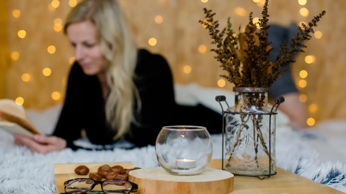 Autumn decoration with candles and a 
pine cone in the foreground. A woman takes a break and reads a book. Fairy lights in the background