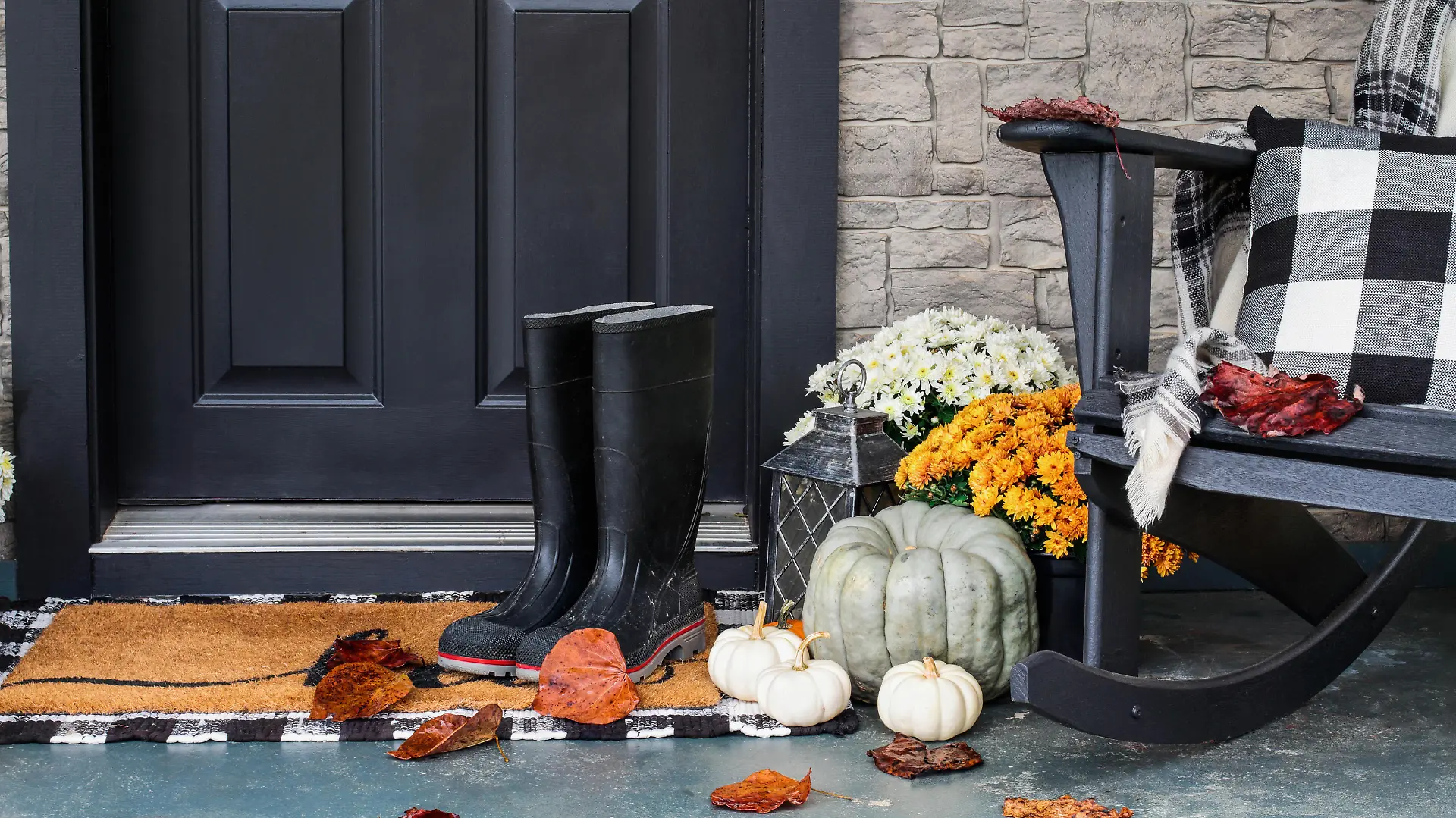 Traditional style front porch decorated for autumn with rain boots, heirloom gourds,  white pumpkins, mums and rocking chair with buffalo plaid pillow and throw blanket giving an inviting atmosphere.