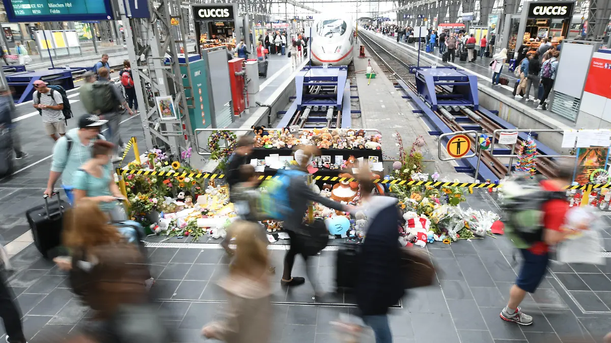 ARCHIV - 20.08.2019, Hessen, Frankfurt/Main: Passanten gehen am Gleis 7 des Hauptbahnhofs an einer Gedenkstelle vorbei, an der sich Blumen, Kuscheltiere und Beileidsbekundungen angesammelt haben (Aufnahme mit längerer Verschlusszeit). Am 29. Juli 2019 wurden ein acht Jahre alter Junge und seine Mutter in das Gleisbett gestoßen. Die Frau konnte sich gerade noch zur Seite retten, ihr Sohn wurde von einem ICE erfasst und starb. (zu dpa «Voraussichtlich Urteilsverkündung um tödliche Gleisattacke») Foto: Arne Dedert/dpa +++ dpa-Bildfunk +++