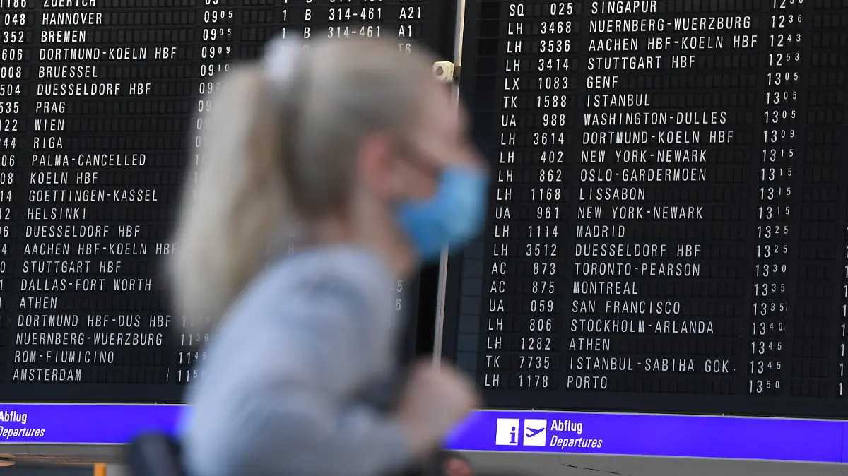 ARCHIV - 15.06.2020, International, Frankfurt/Main: Eine Frau, die einen Mundschutz trägt, steht im Terminal 1 des Frankfurter Flughafens in der Abflughalle vor einer großen Anzeigetafel. Die Bundesregierung hat die Reisewarnung wegen der Corona-Pandemie für mehr als 160 Länder außerhalb der Europäischen Union um zwei Wochen bis zum 14. September 2020 verlängert. Foto: Arne Dedert/dpa +++ dpa-Bildfunk +++