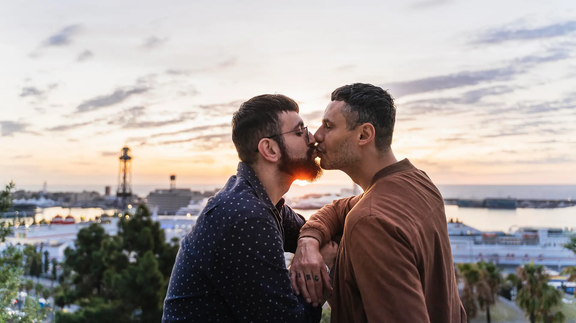 Gay couple kissing on lookout above the city with view to the port, Barcelona, Spain || Modellfreigabe vorhanden
