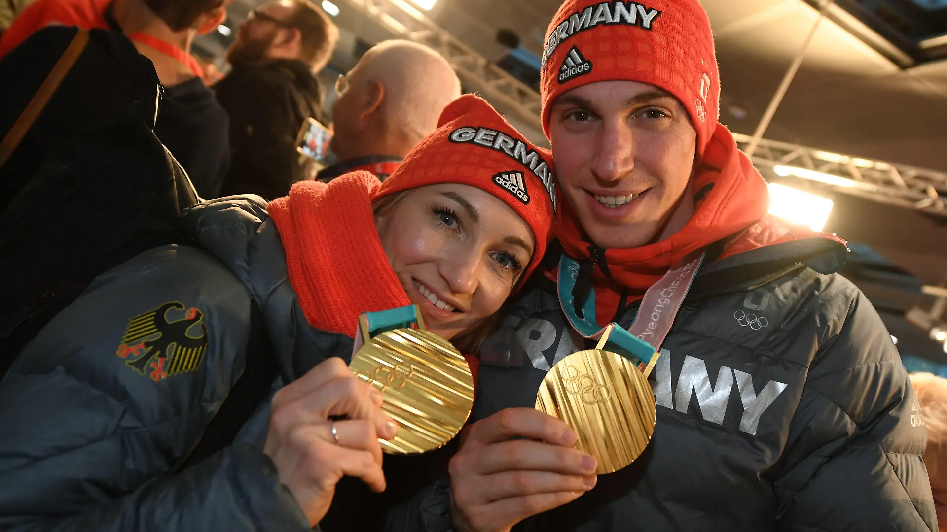 26.02.2018, Hessen, Frankfurt am Main: das Eiskunstlaufpaar Aljona Savchenko (r-l) und Bruno Massot wird nach der Landung der Lufthansa-Maschine LH713 mit mehr als 150 Sportlern, Trainern und Funktionären an Bord von Fans begrüßt und zeigt seine Goldmedaillen. Foto: Arne Dedert/dpa +++ dpa-Bildfunk +++