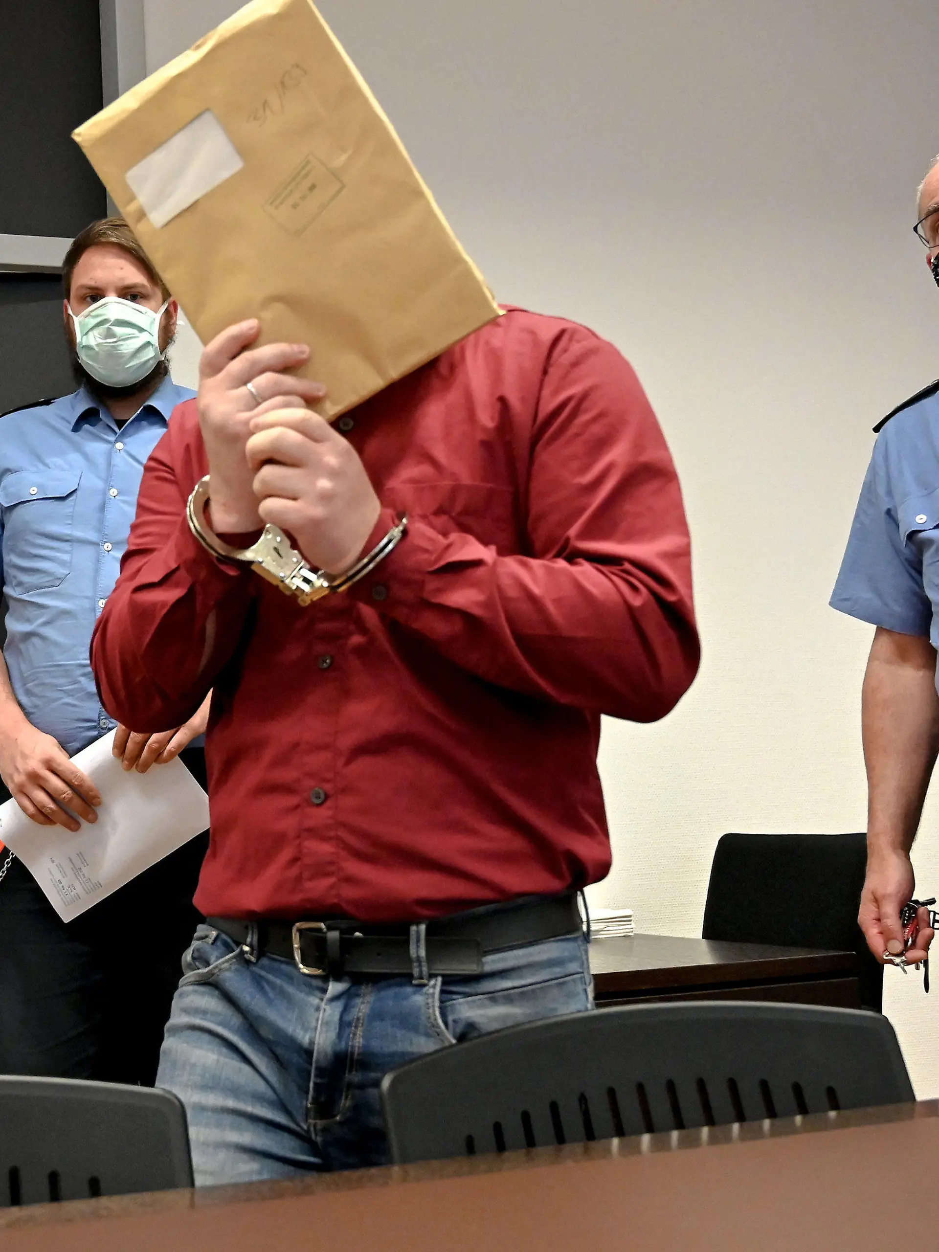 25.08.2020, Hessen, Wiesbaden: Der Angeklagte betritt, von Justizbeamten begleitet, in Handschellen den Gerichtssaal des Landgerichts und verbirgt sein Gesicht. Dem 39-jährigen Angeklagten wird vorgeworfen, seine leiblichen Kinder, darunter einen Säugling und ein Stiefkind, sexuell missbraucht und Bilder der Verbrechen über Chatgruppen verschickt zu haben. Die Ermittlungen zu dem Fall waren nach Durchsuchungen bei einem 43 Jahre alten Familienvater im nordrhein-westfälischen Bergisch Gladbach im Herbst 2019 ins Rollen gekommen. Foto: Sascha Steinbach/epa/Pool/dpa +++ dpa-Bildfunk +++