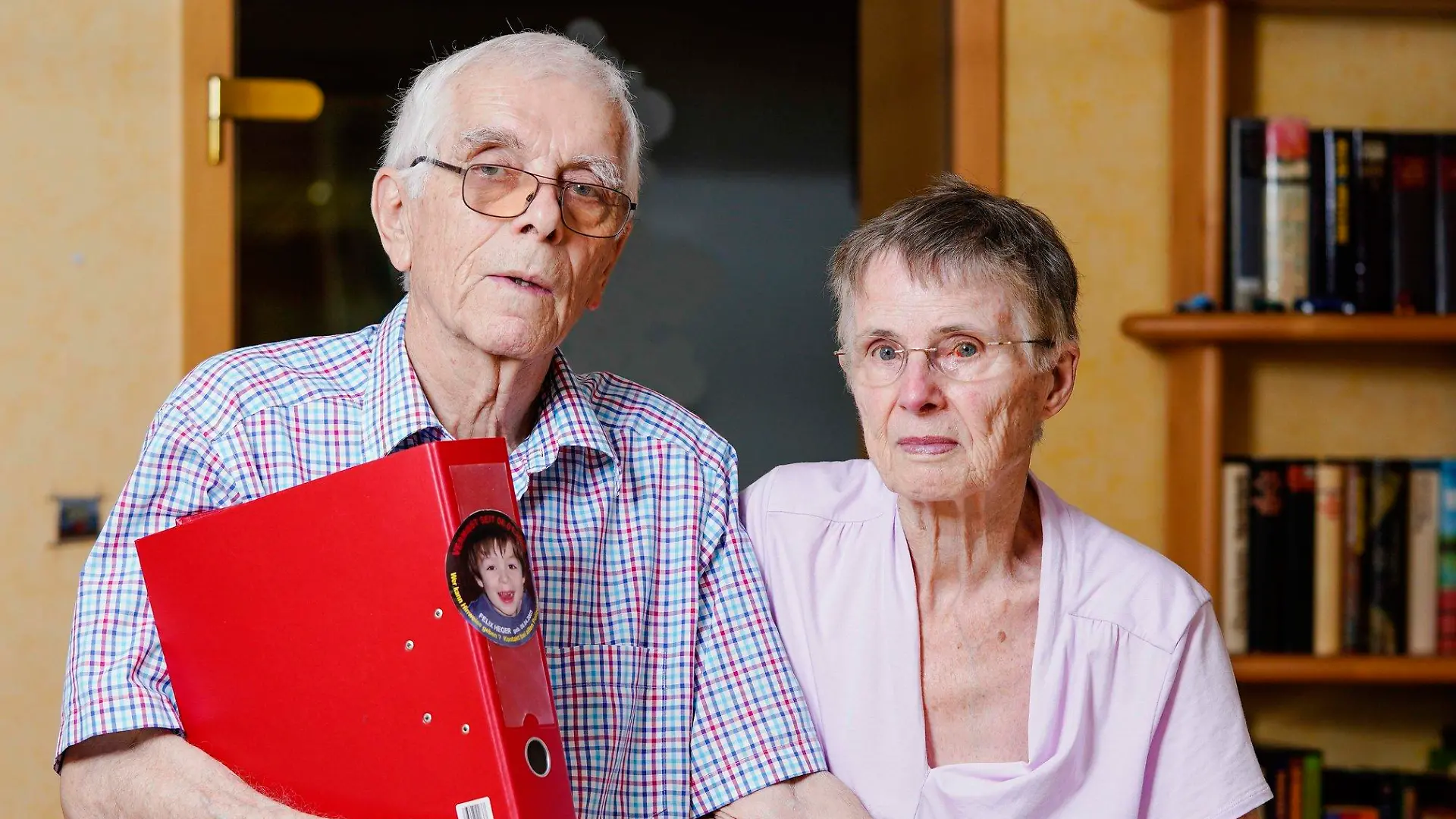 14.08.2020, Baden-Württemberg, Schwetzingen: Johann und Maria Schmitz, Großeltern des seit rund 14 Jahren vermissten Felix Heger, stehen im Wohnzimmer ihres Hauses und halten einen roten Aktenordner mit dem Bild des zweijährigen Kindes in den Händen. (zu dpa «Wo ist Felix? Großeltern suchen seit 14 Jahren nach vermisstem Enkel») Foto: Uwe Anspach/dpa +++ dpa-Bildfunk +++