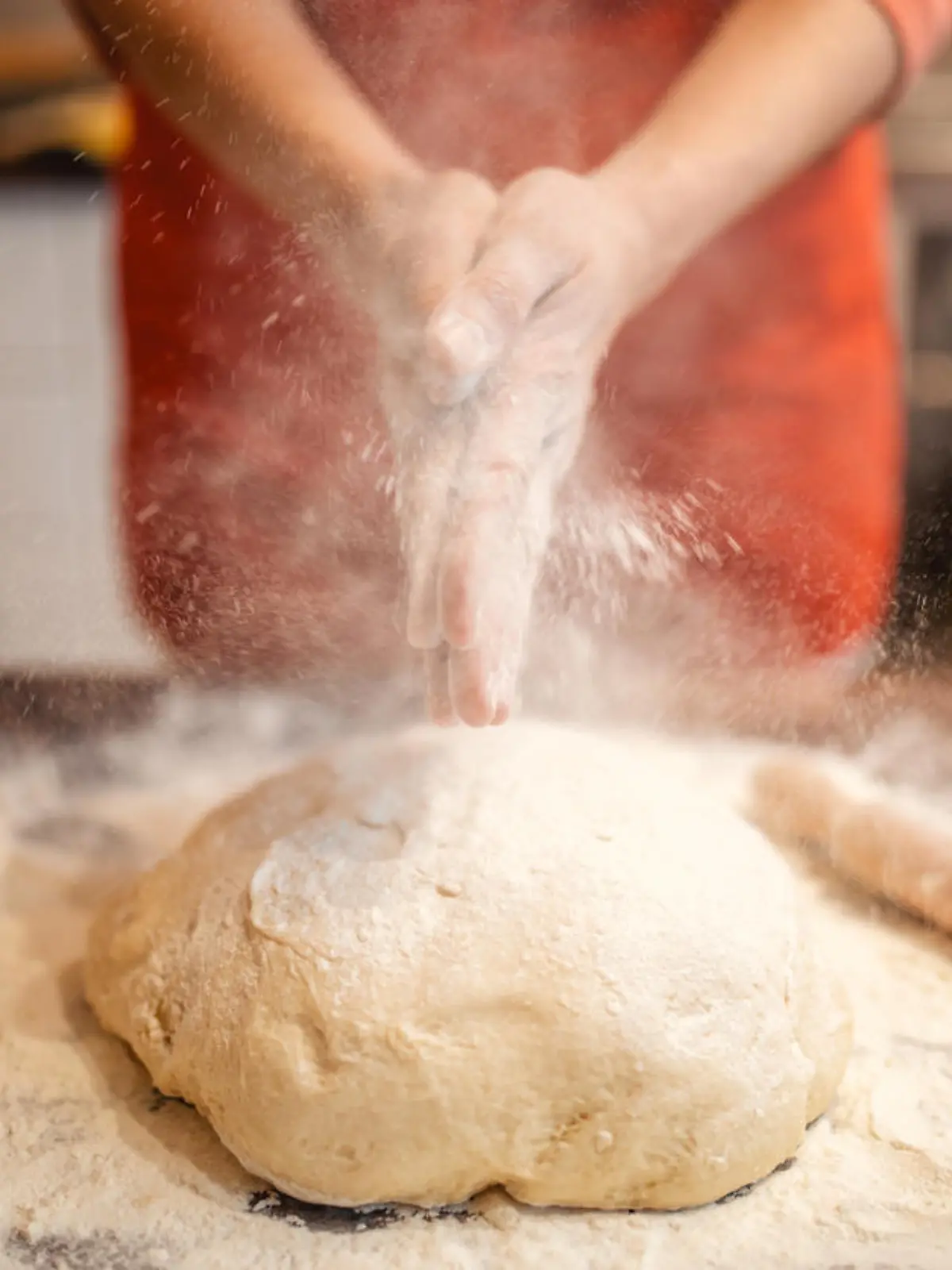 Woman preparing and kneading dough for bread and cakes. She wears a red apron and works in her kitchen. She is unrecognizable