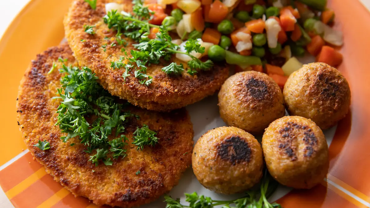 Vegane Falafel, vegane Schnitzel und Gemüse sind auf einem Teller in einer Küche zu sehen.