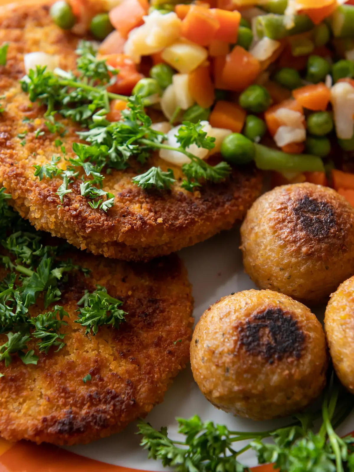 Vegane Falafel, vegane Schnitzel und Gemüse sind auf einem Teller in einer Küche zu sehen.