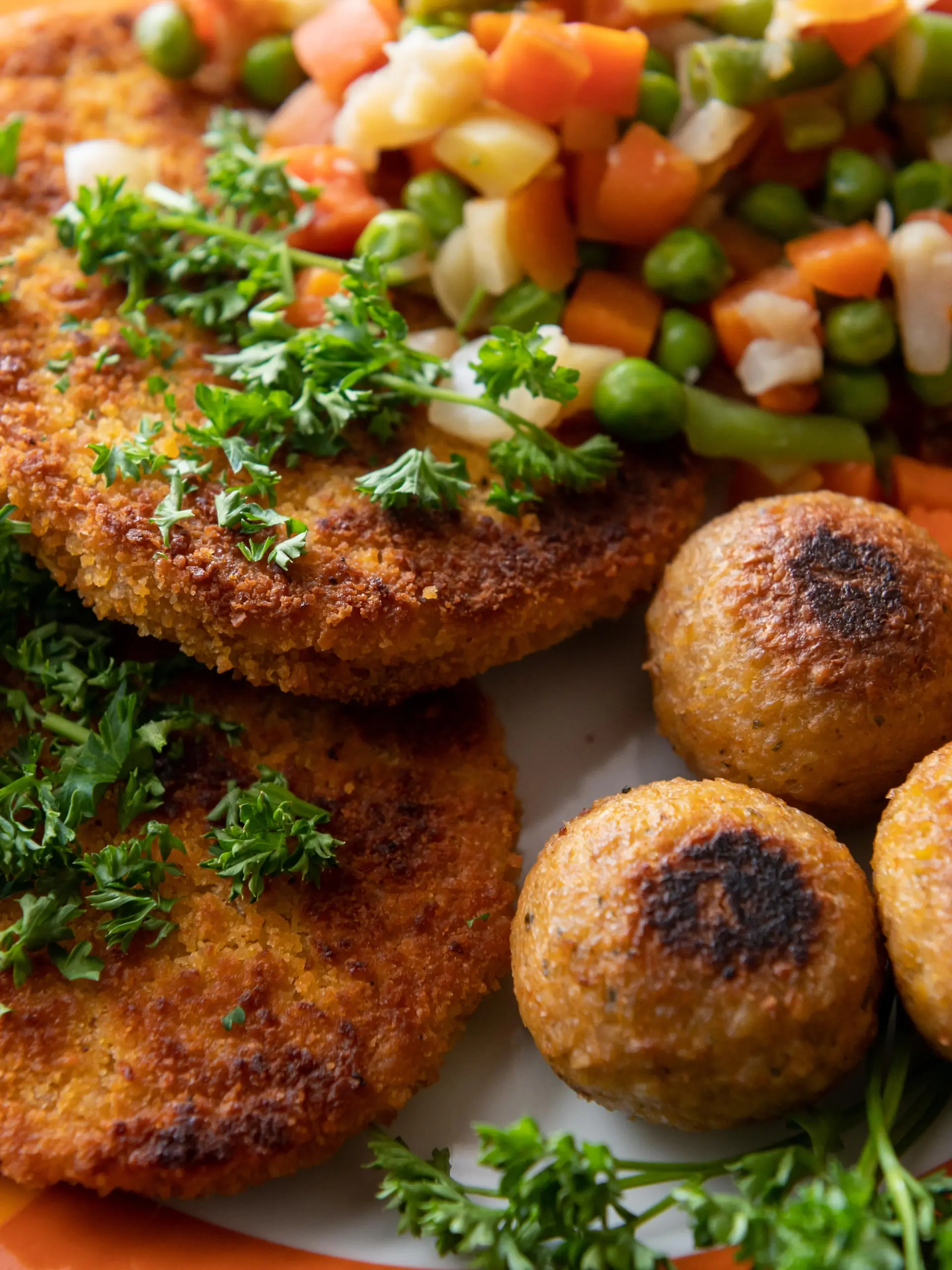 Vegane Falafel, vegane Schnitzel und Gemüse sind auf einem Teller in einer Küche zu sehen.