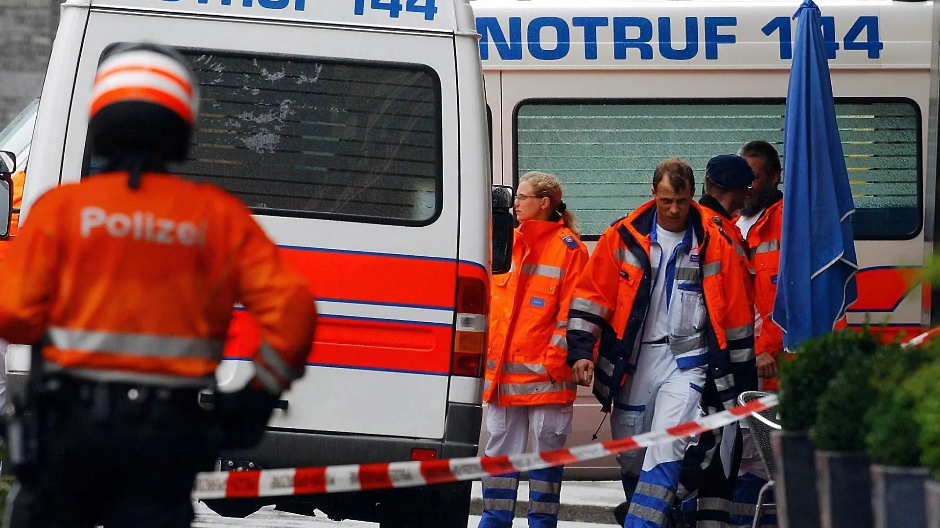 Angehörige der Zürcher Polizei und Sanitäter warten am Montag (05.07.2004) vor dem Bürogebäude der Zürcher Kantonalbank (ZKB) am Tessinerplatz in Zürich, nachdem es in den Räumlichkeiten der ZKB am Morgen zu einer Schießerei gekommen war. Ein Finanzberater ist dort Amok gelaufen und hat zwei seiner Vorgesetzten angeschossen. Anschließend tötete er sich selbst. Das teilte die Polizei mit. Die Opfer des 56-Jährigen sind der Leiter der Finanzplanung und der Leiter der Finanzberatung. Der Täter war an seinem Arbeitsplatz am Tessinerplatz erschienen und hatte kurz darauf zu feuern begonnen. Foto: Walter Bieri dpa
