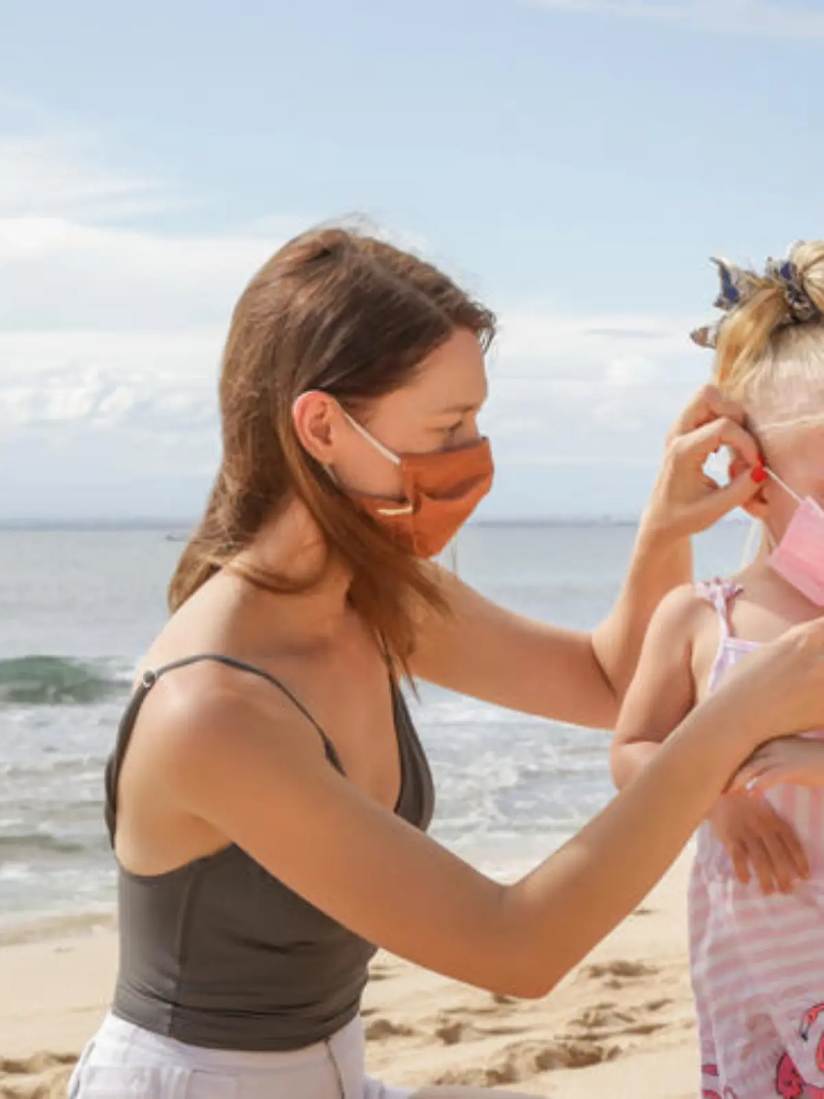 Eine Mutter zieht ihrem Kind am Strand die Maske an zum Schutz vor Covid-19