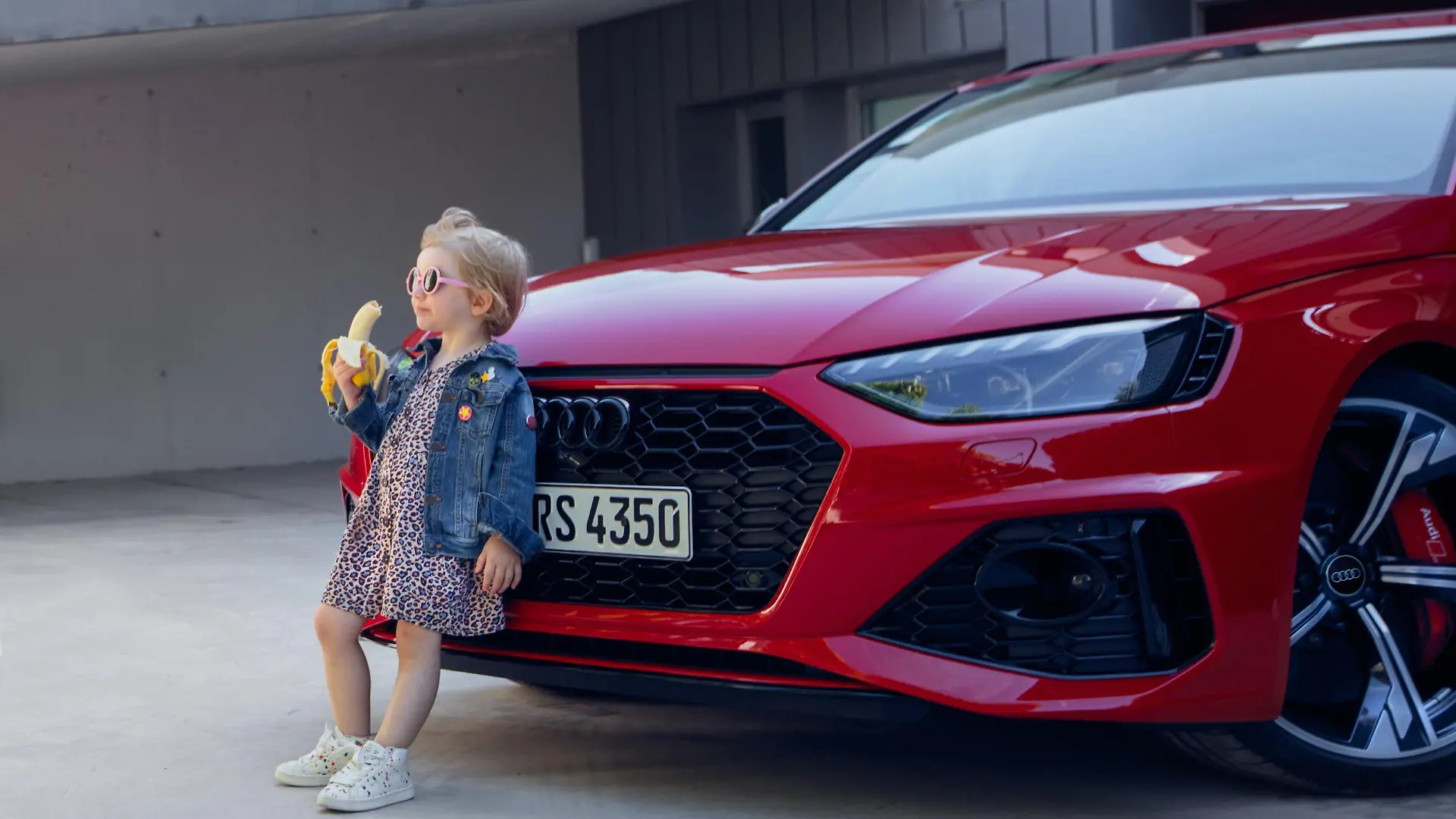 Audi-Werbekampagne: Ein kleines Mädchen steht, Banane-essend, vor dem Kühlergrill eines Autos.