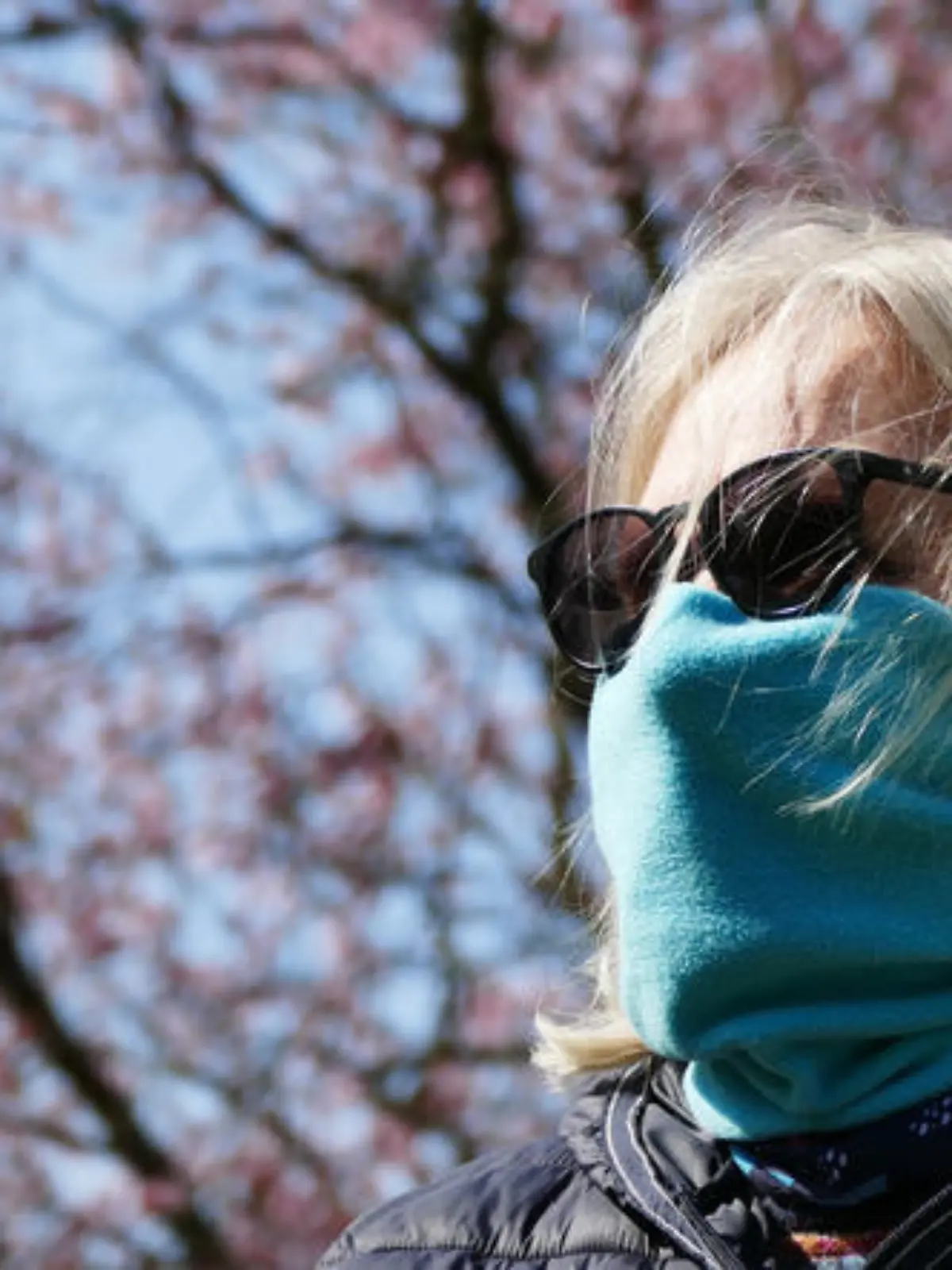 Frau hat eine Sonnenbrille auf und trägt einen Schal vor dem Mund