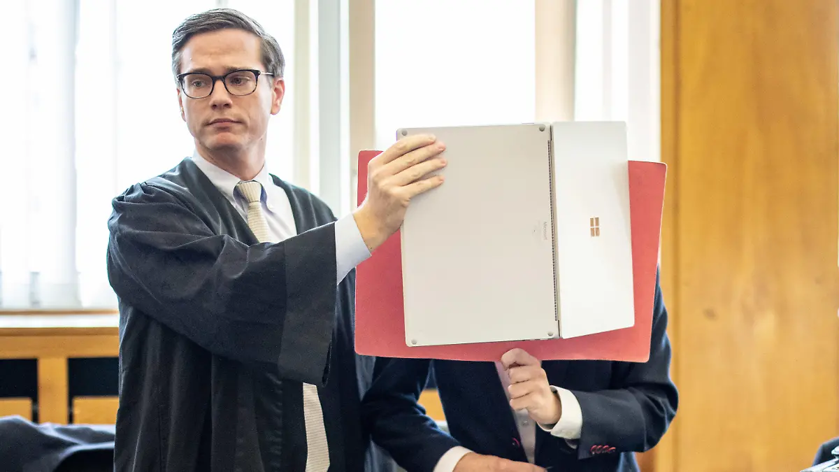 03.08.2020, Nordrhein-Westfalen, Essen: Der Angeklagte (r) steht im Gerichtssaal mit einer Mappe vor dem Gesicht neben seinem Anwalt Roland Rautenberger. Wegen fahrlässiger Tötung ist der 25-jährige Fahrer angeklagt. Er soll einen Fahrfehler mit einem Sportwagen bei Tempo 300 im März 2019 gemacht haben. Bei dem Unfall starb seine 18-jährige Beifahrerin. Foto: Marcel Kusch/dpa +++ dpa-Bildfunk +++