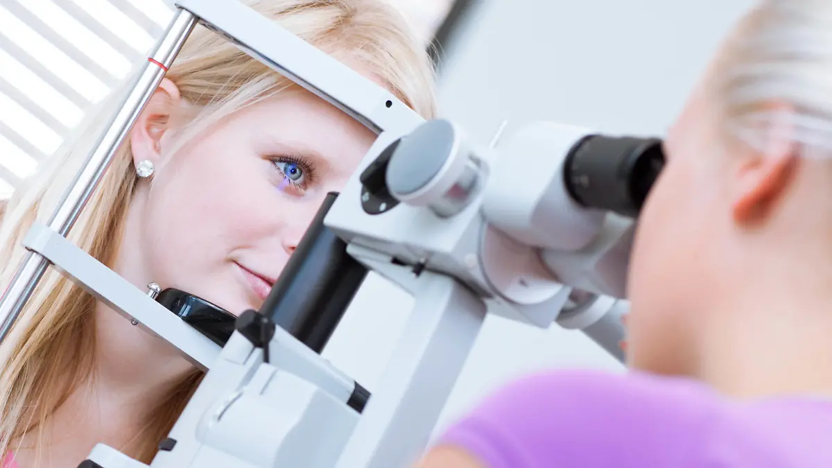 optometry concept - pretty, young female patient having her eyes examined by an eye doctor (color toned image; shallow DOF) | Verwendung weltweit, Keine Weitergabe an Wiederverkäufer.