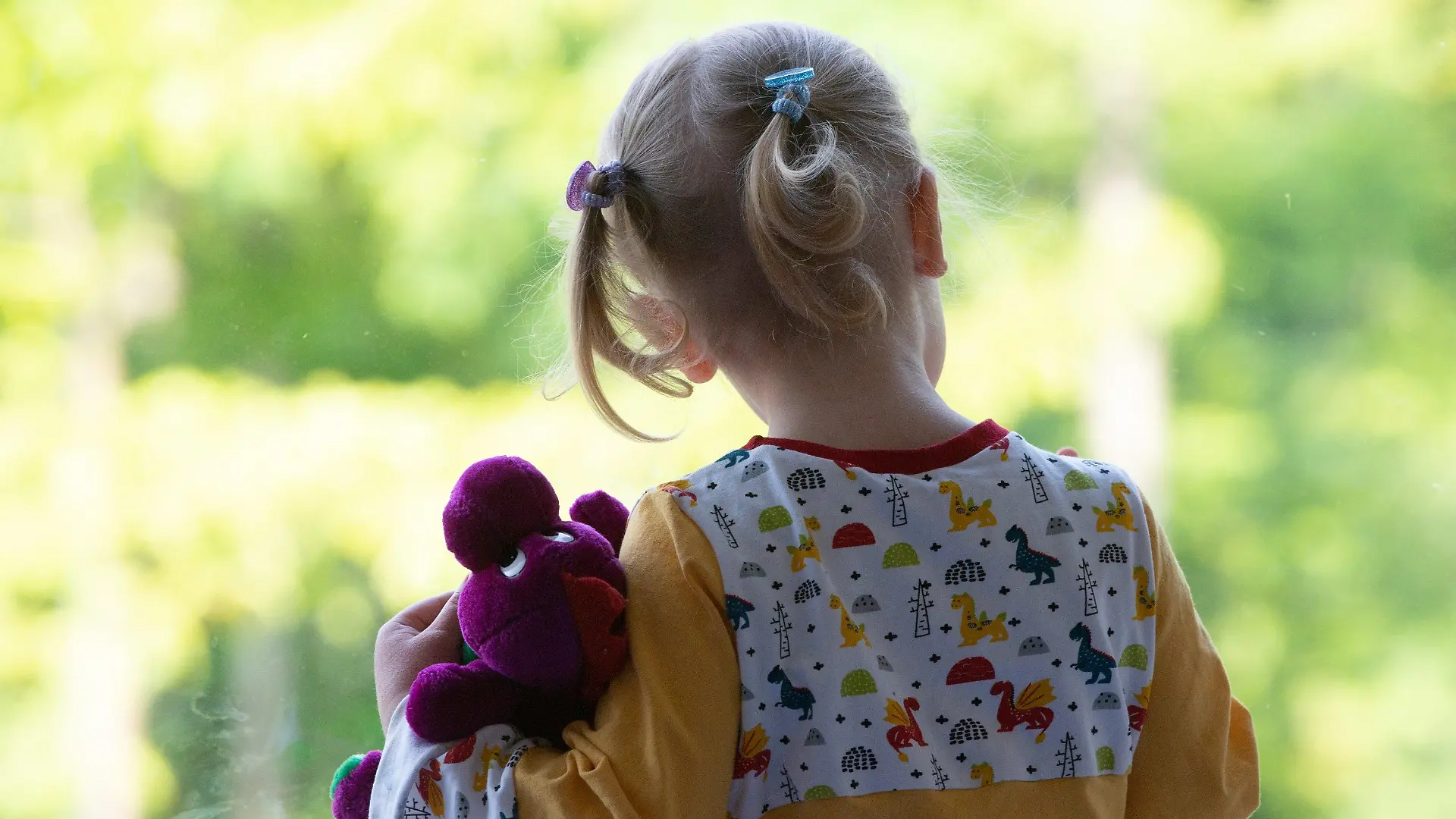 18.05.2020, Sachsen, Dresden: Ein Kind steht in einem Kindergarten mit einem Kuscheltier an einer Fensterscheibe. Nach wochenlanger Corona-Zwangspause dürfen Kinder nun wieder in die Krippen und Kitas. Foto: Sebastian Kahnert/dpa-Zentralbild/dpa +++ dpa-Bildfunk +++