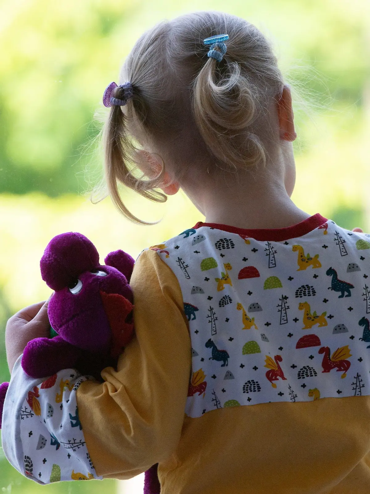 18.05.2020, Sachsen, Dresden: Ein Kind steht in einem Kindergarten mit einem Kuscheltier an einer Fensterscheibe.  Nach wochenlanger Corona-Zwangspause dürfen Kinder nun wieder in die Krippen und Kitas. Foto: Sebastian Kahnert/dpa-Zentralbild/dpa +++ dpa-Bildfunk +++