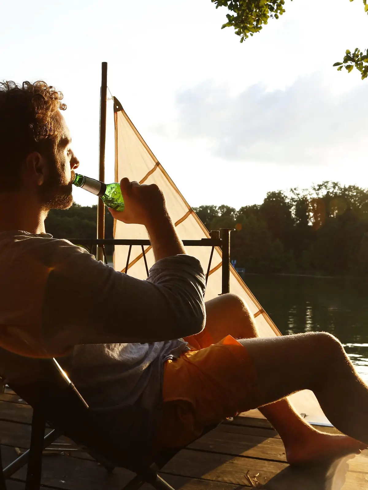 Young man with drinking a beer on a jetty next to sailing boat model released Symbolfoto PUBLICATIONxINxGERxSUIxAUTxHUNxONLY FKF02847  