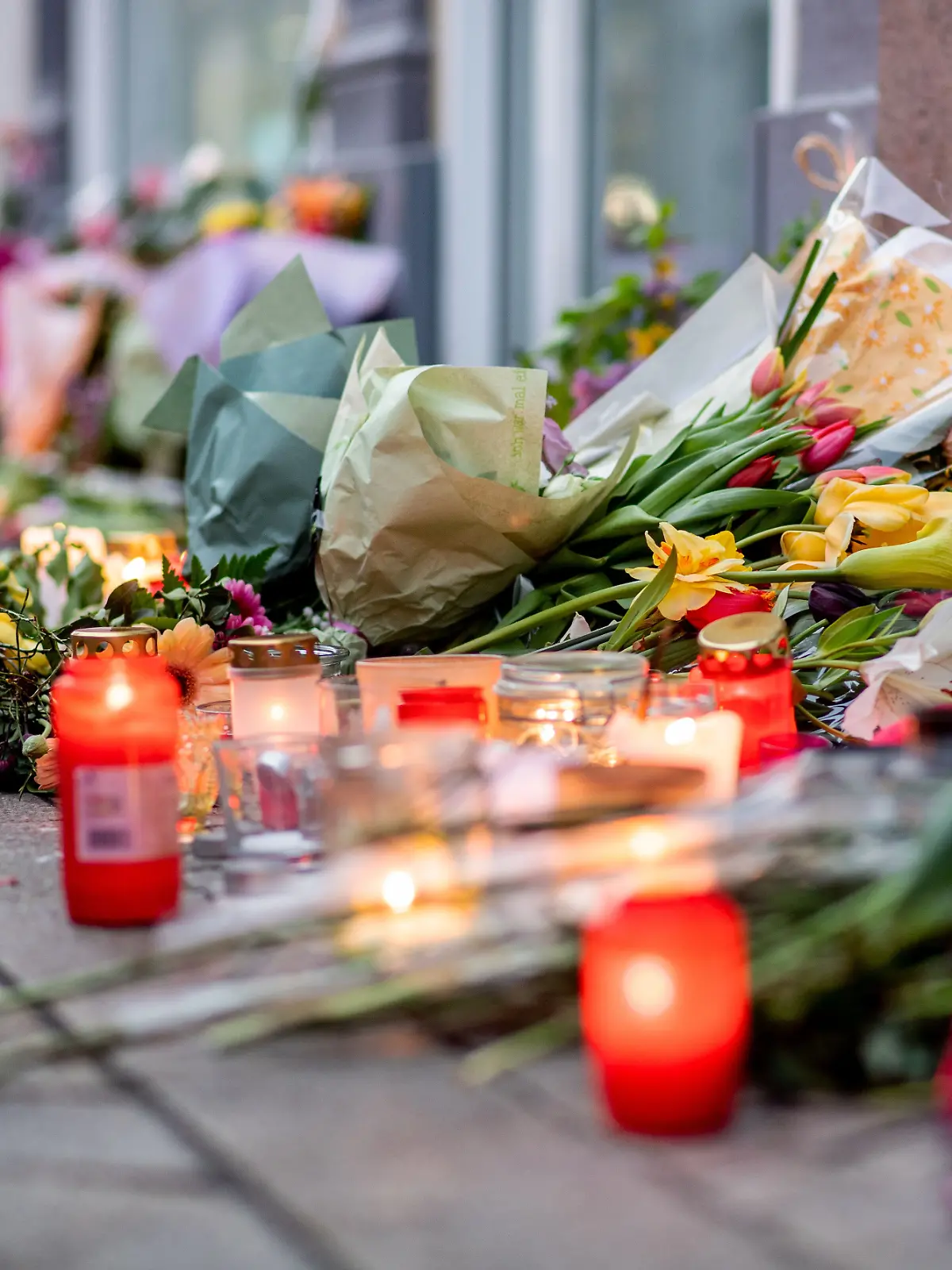 22.04.2025, Niedersachsen, Oldenburg: Zahlreiche Blumen und Kerzen stehen in der Innenstadt an einer Hauswand in der Achternstraße, in der am frühen Sonntagmorgen ein Mensch von Schüssen aus einer Polizeiwaffe tödlich verletzt wurde. Der 21-Jährige hatte zuvor vor einer Diskothek Reizgas versprüht und mehrere Menschen leicht verletzt. Foto: Hauke-Christian Dittrich/dpa +++ dpa-Bildfunk +++