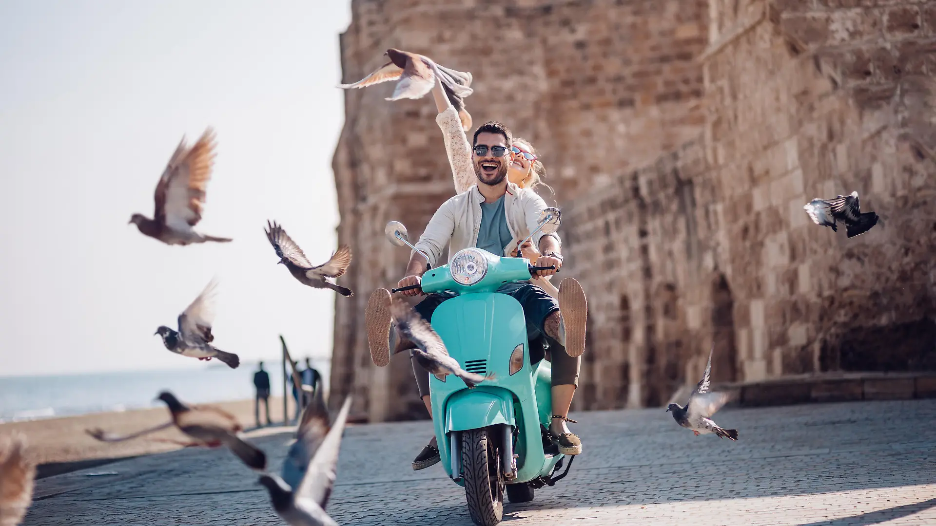 Pärchen, das mit einem Motorroller am Meer entlang fährt.