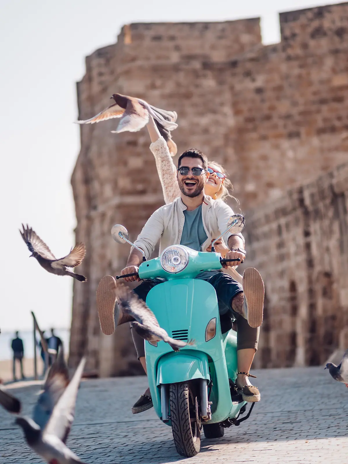Pärchen, das mit einem Motorroller am Meer entlang fährt.