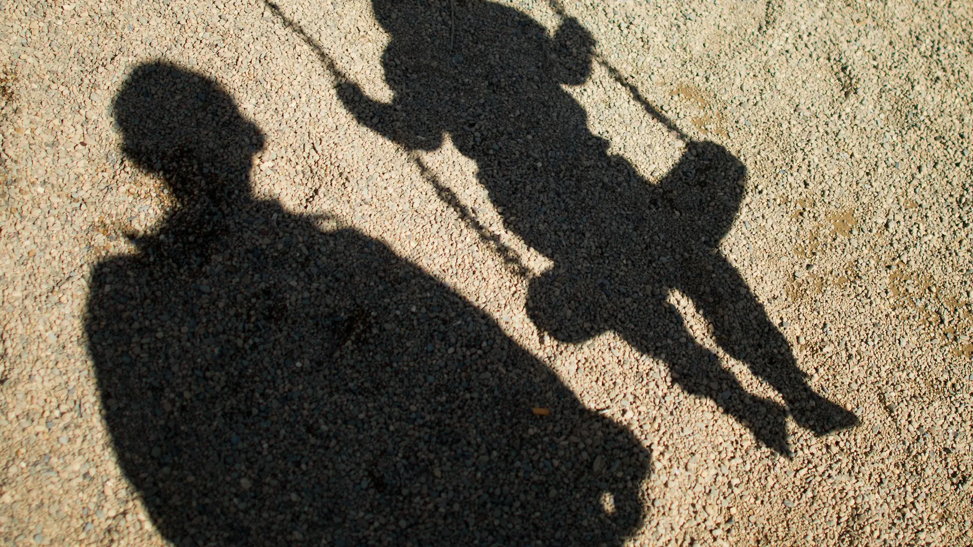ARCHIV - ILLUSTRATION - Der Schatten von einem Mann und einem schaukelnden Kind fallen am 27.08.2014 auf Sand auf einem Spielplatz in Braunschweig (Niedersachsen). Foto: Julian Stratenschulte/dpa (zu dpa «Mann soll Jugendliche missbraucht haben - Neonazi als Vermittler» vom 05.11.2014) +++(c) dpa - Bildfunk+++