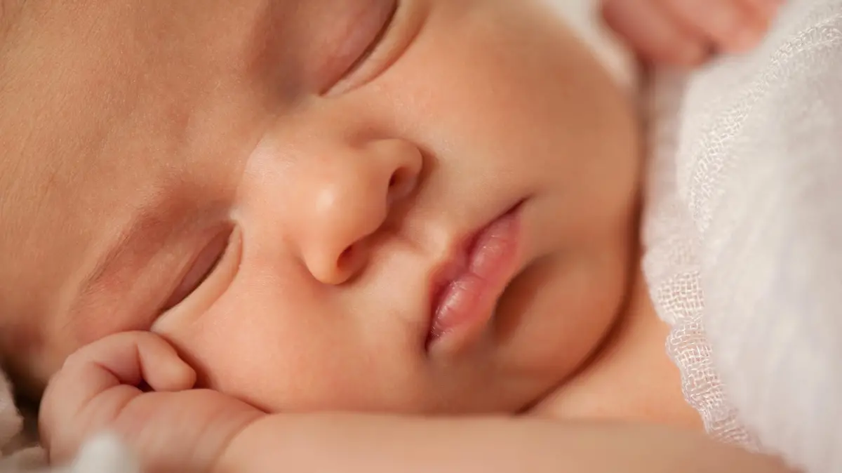 A close-up photograph of a sleeping newborn baby's face. It's a selective focus image, with the focus being on the infant's tiny lips.