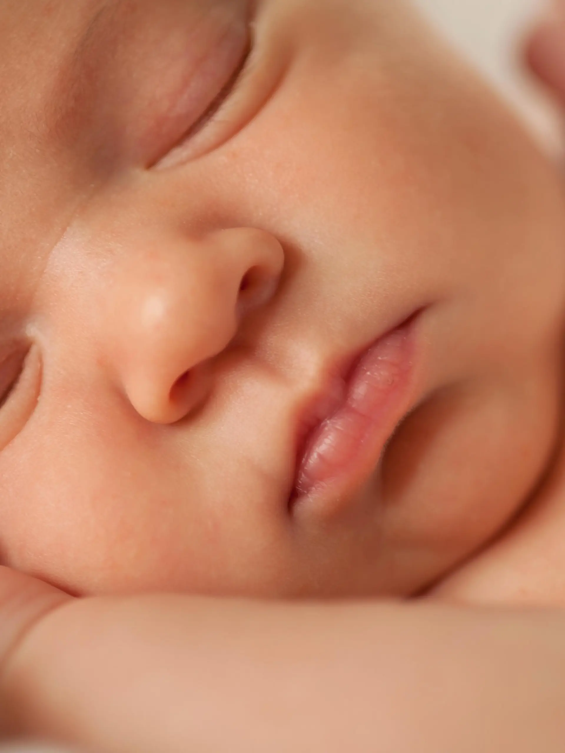 A close-up photograph of a sleeping newborn baby's face. It's a selective focus image, with the focus being on the infant's tiny lips.
